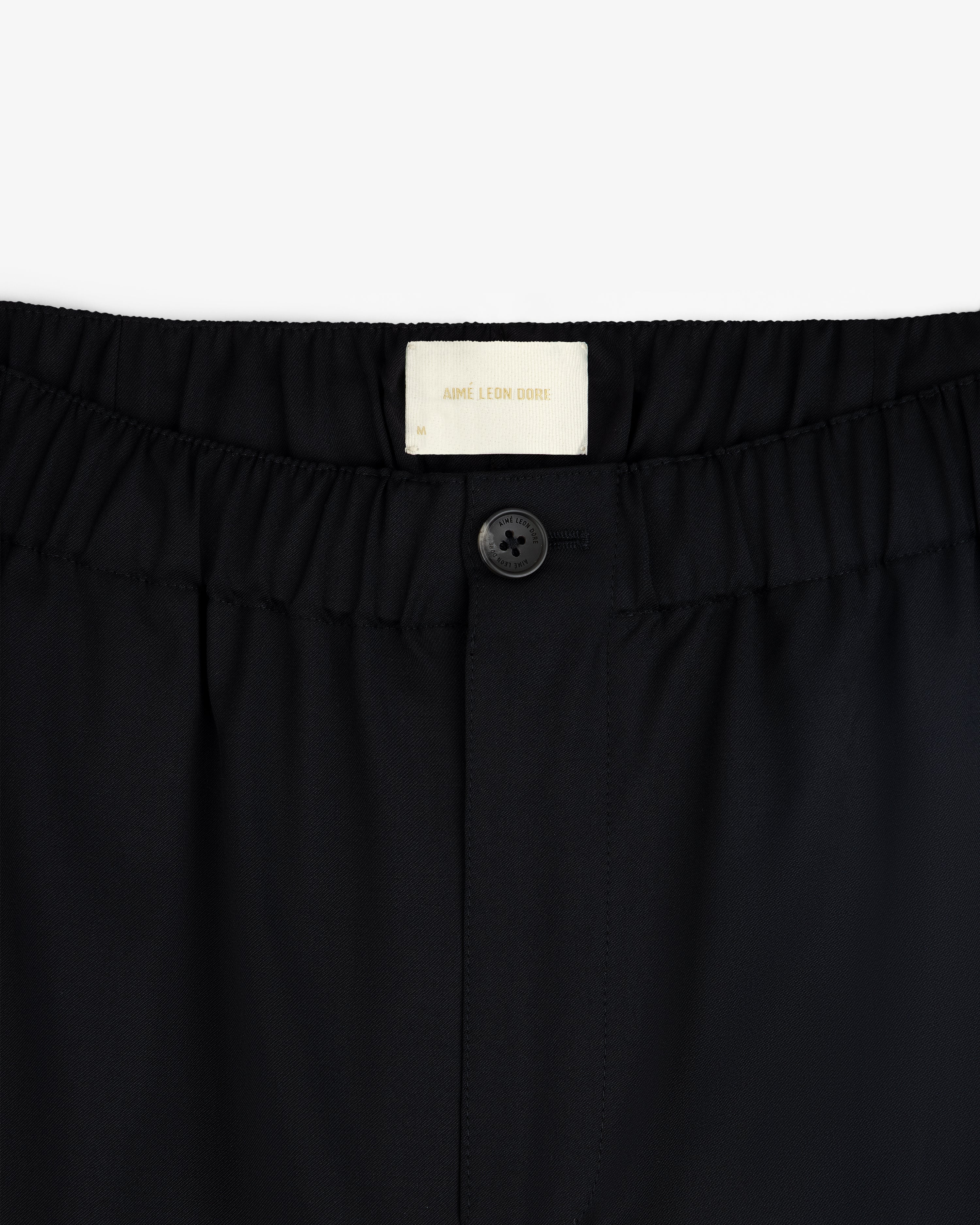 Close-up of Elasticated Waist Gabardine Trouser in black with an elastic waistband, button, and visible white label inside.