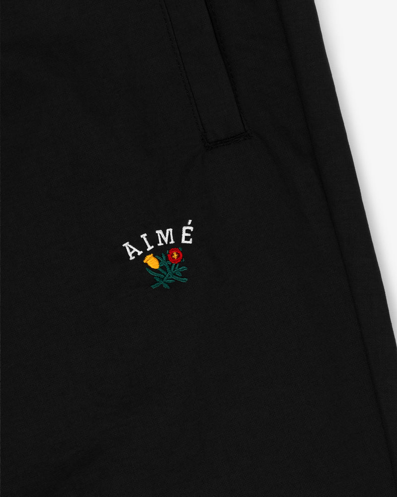 Close-up of black Crest Nylon Track Pant with AIMÉ and two embroidered flowers, yellow and red, below pocket seam.