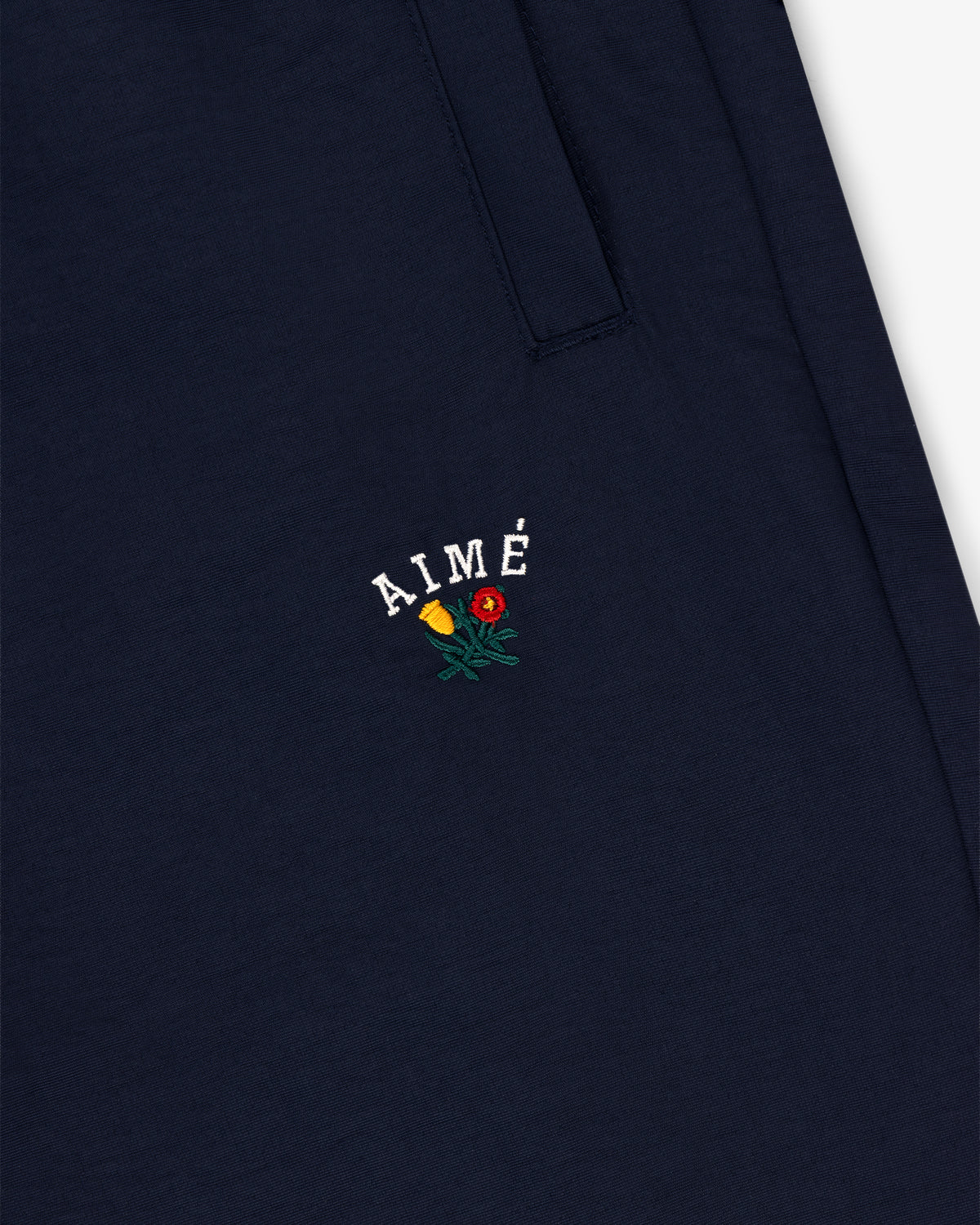 Navy blue Crest Nylon Track Pant with AIMÉ and small yellow and red flower embroidery below the pocket.