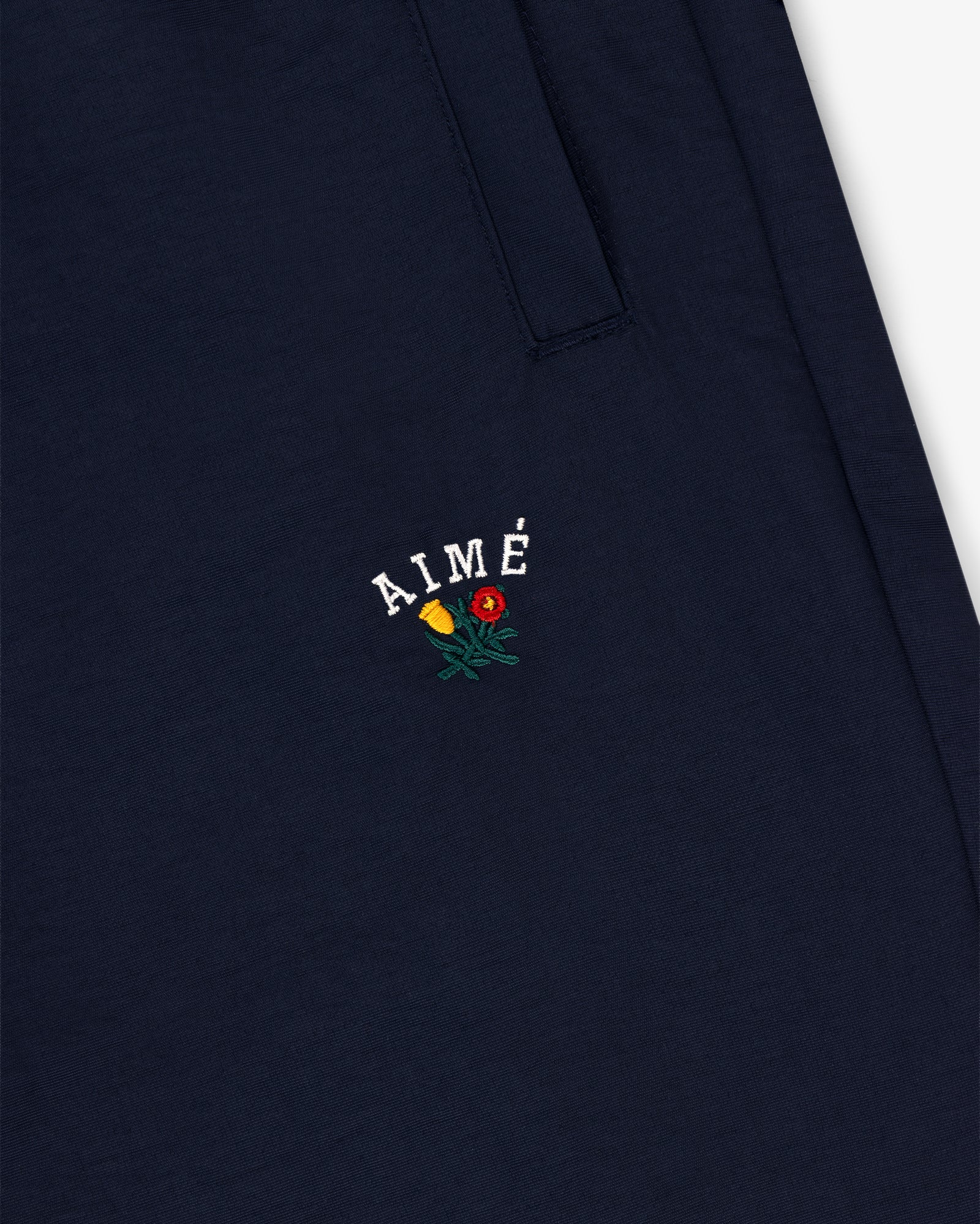 Navy blue Crest Nylon Track Pant with AIMÉ and small yellow and red flower embroidery below the pocket.