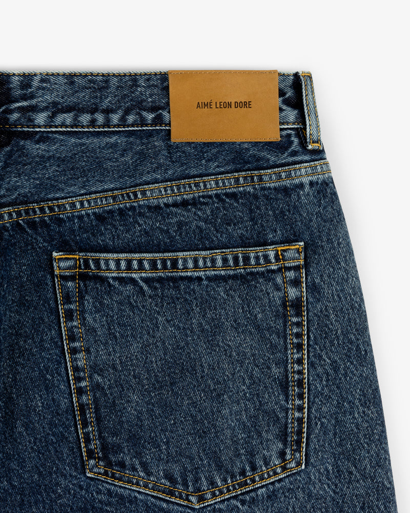 Close-up of Relaxed Fit 5-Pocket Denim Pant in blue with brown leather AIMÉ LEON DORE patch above back pocket.