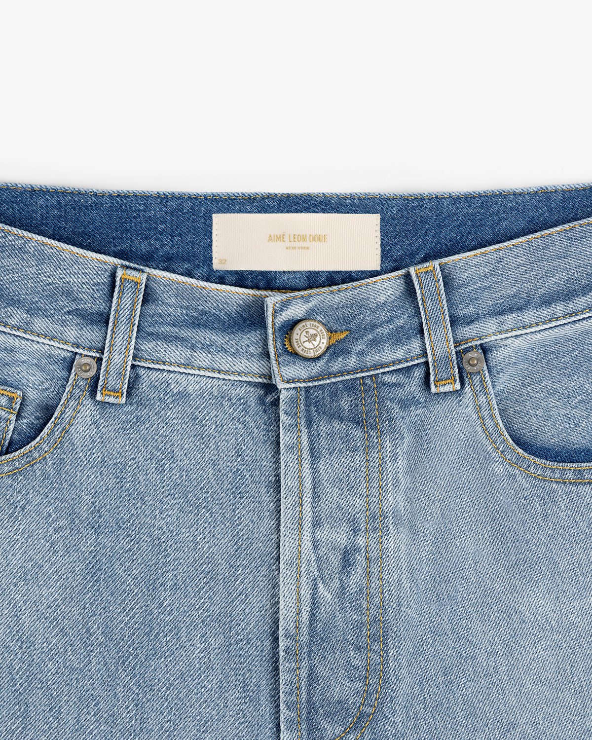 Close-up of the waist and button of Relaxed Fit 5-Pocket Denim Pant in light blue with visible inner white label.