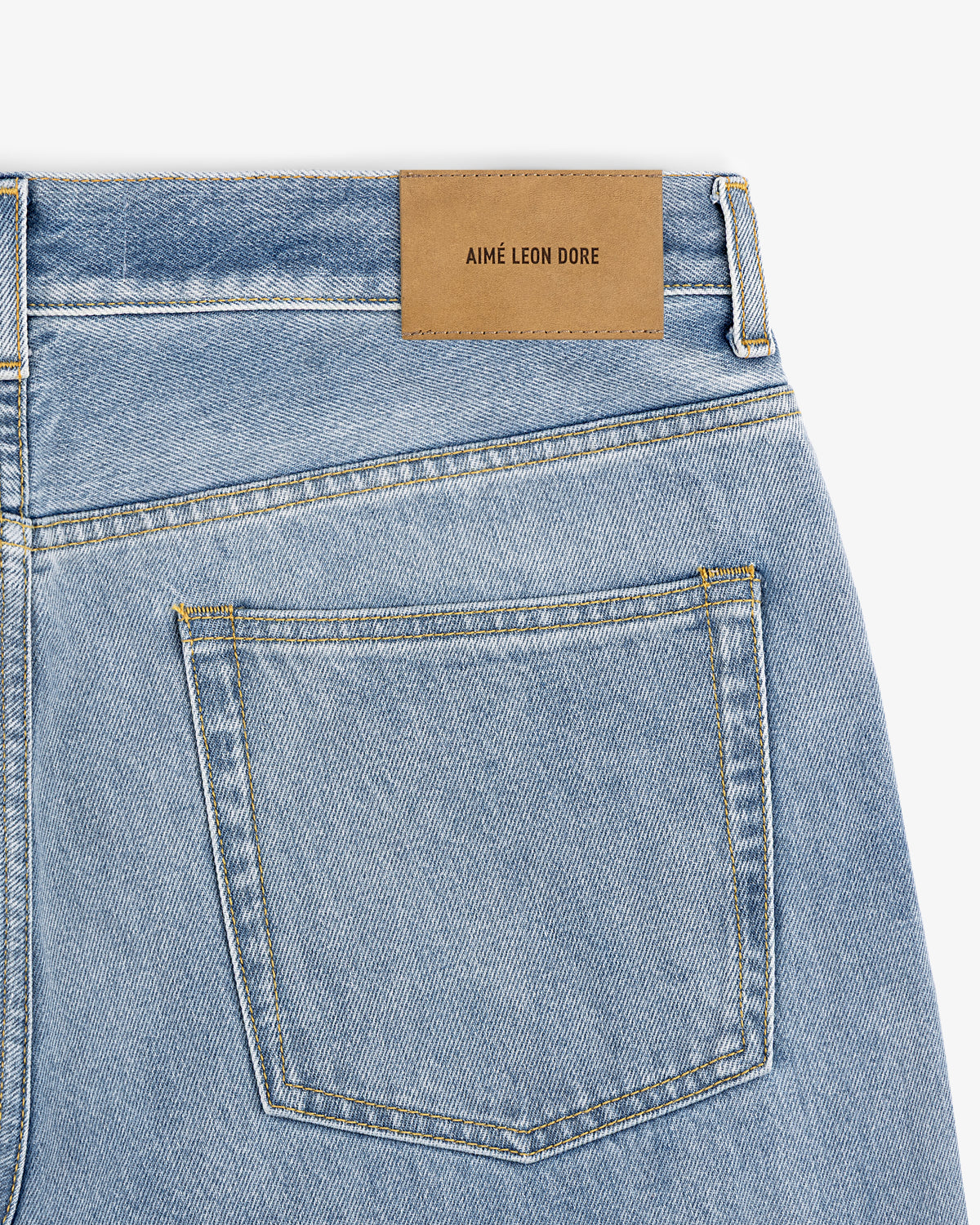 Close-up of light blue Relaxed Fit 5-Pocket Denim Pant with a brown AIMÉ LEON DORE patch above the back pocket.