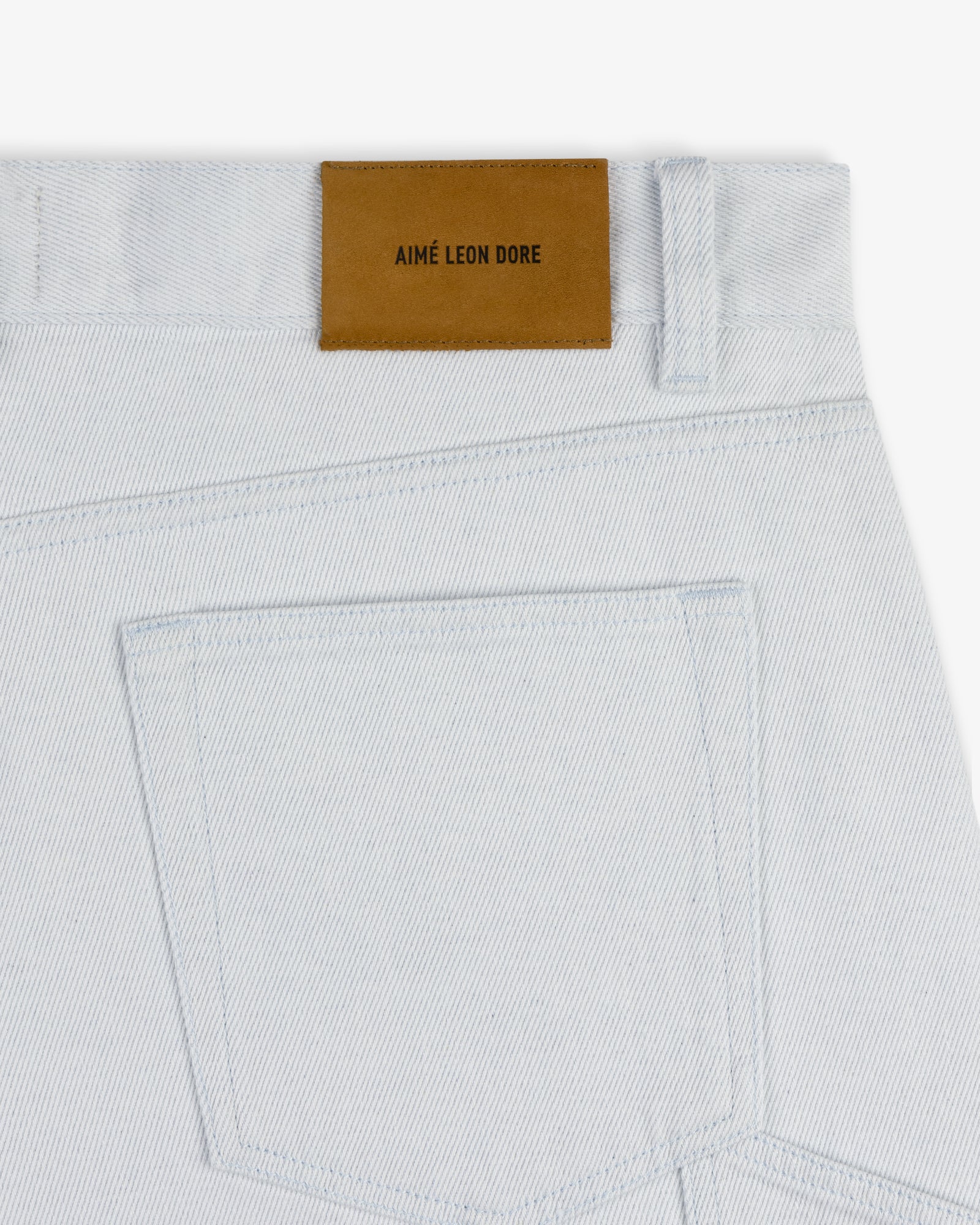 Back pocket of Light Wash Denim Short with a brown leather patch that reads AIMÉ LEON DORE above the waistband.