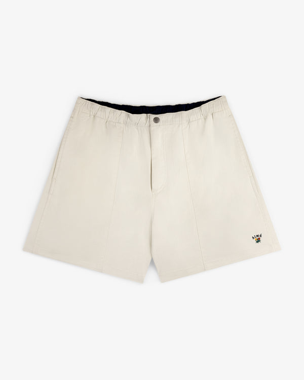 Crest Casual Short in beige with side pockets and a small colorful embroidered logo near the hem.