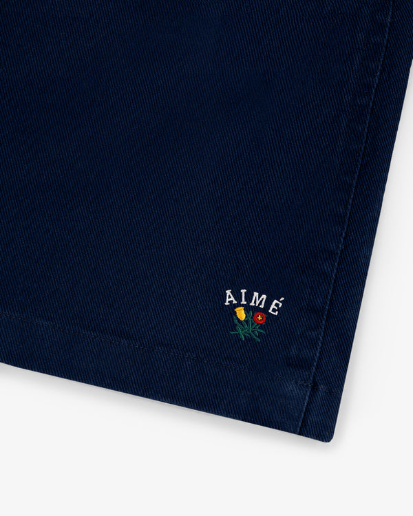 Close-up of Crest Casual Short in navy blue with AIMÉ and small yellow and red embroidered flowers near the corner.
