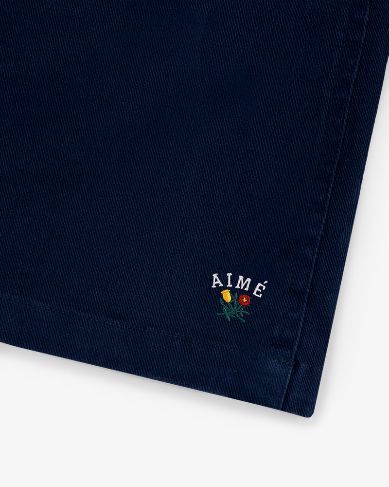 Close-up of Crest Casual Short in navy blue with AIMÉ and small yellow and red embroidered flowers near the corner.