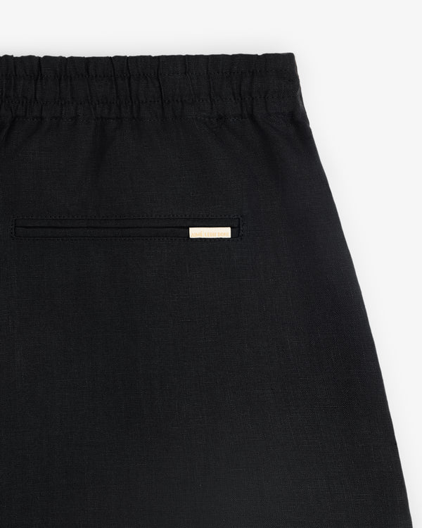 Close-up of the Linen Leisure Short in black with an elastic waistband and a small label above the welt back pocket.