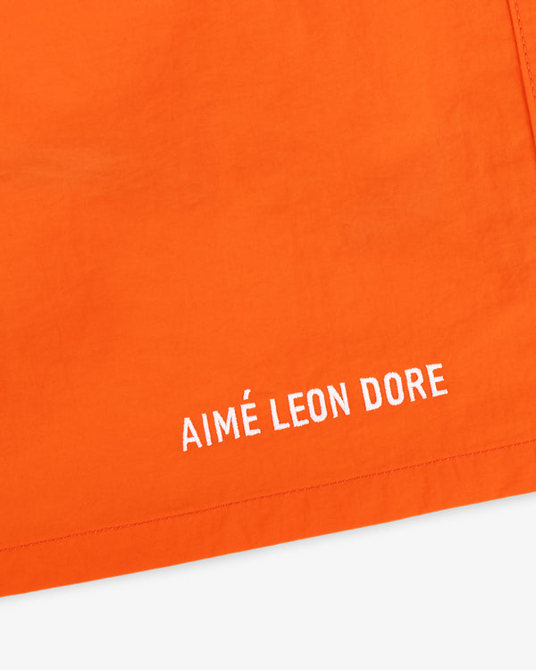 Close-up of orange Logo Swim Short with AIMÉ LEON DORE embroidered in white near the hem.