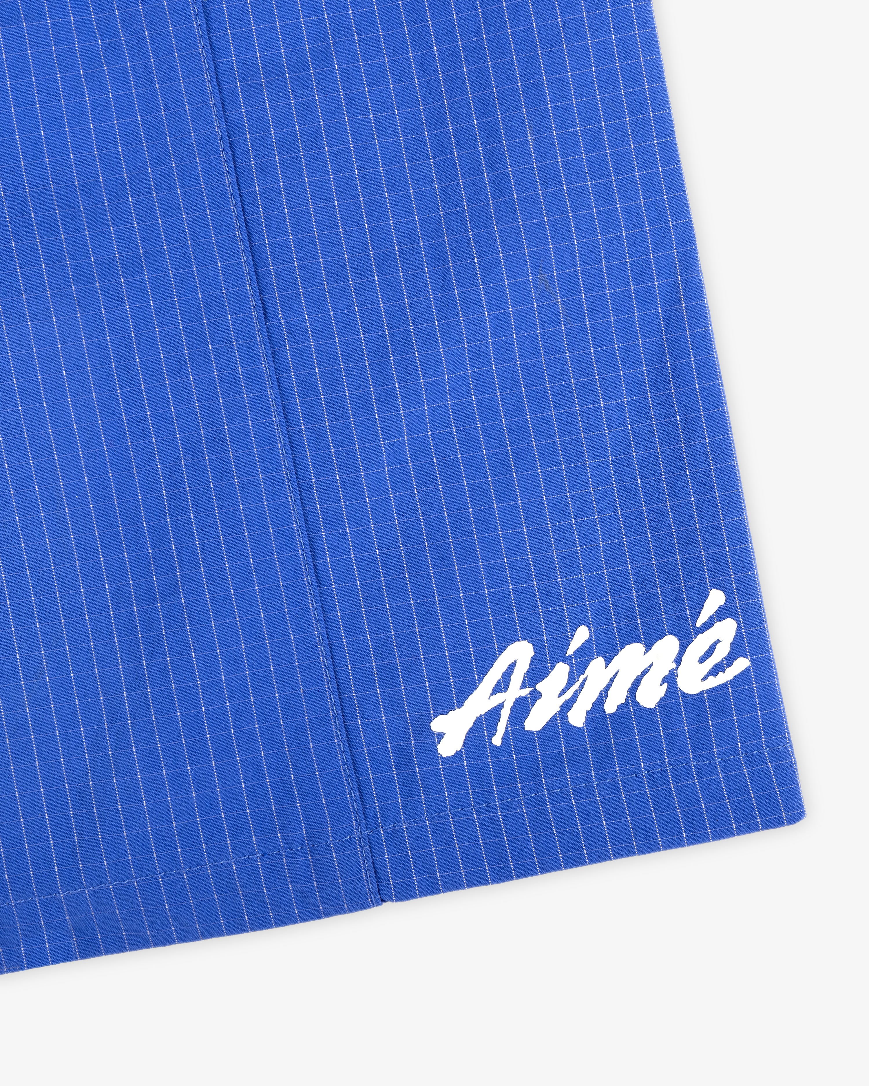 Close-up of blue Ripstop Nylon Wave Short with white grid pattern and Aimé in white script in the corner.