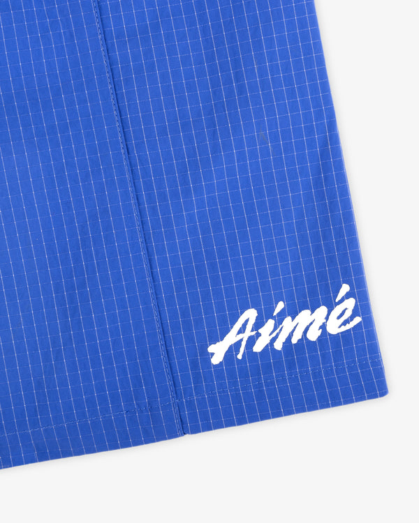 Close-up of blue Ripstop Nylon Wave Short with white grid pattern and Aimé in white script in the corner.