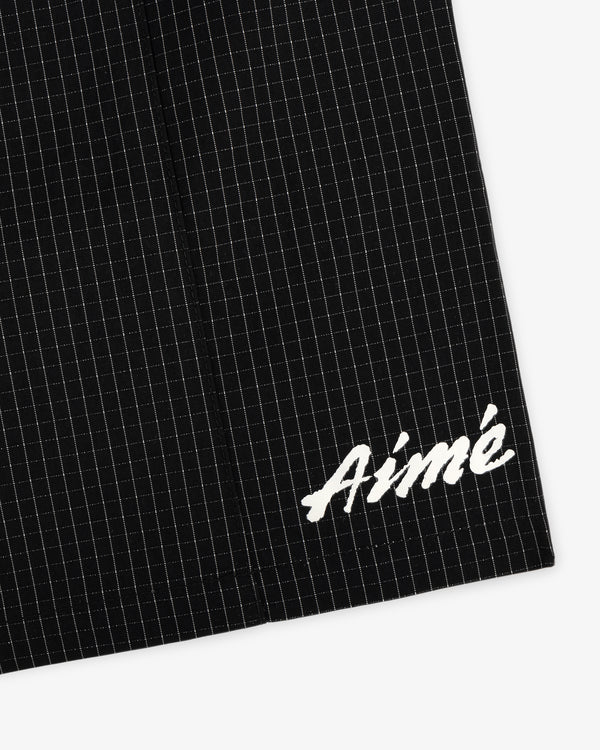 Close-up of Ripstop Nylon Wave Short in black with white grid lines and Aimé embroidered in white script on the lower corner.