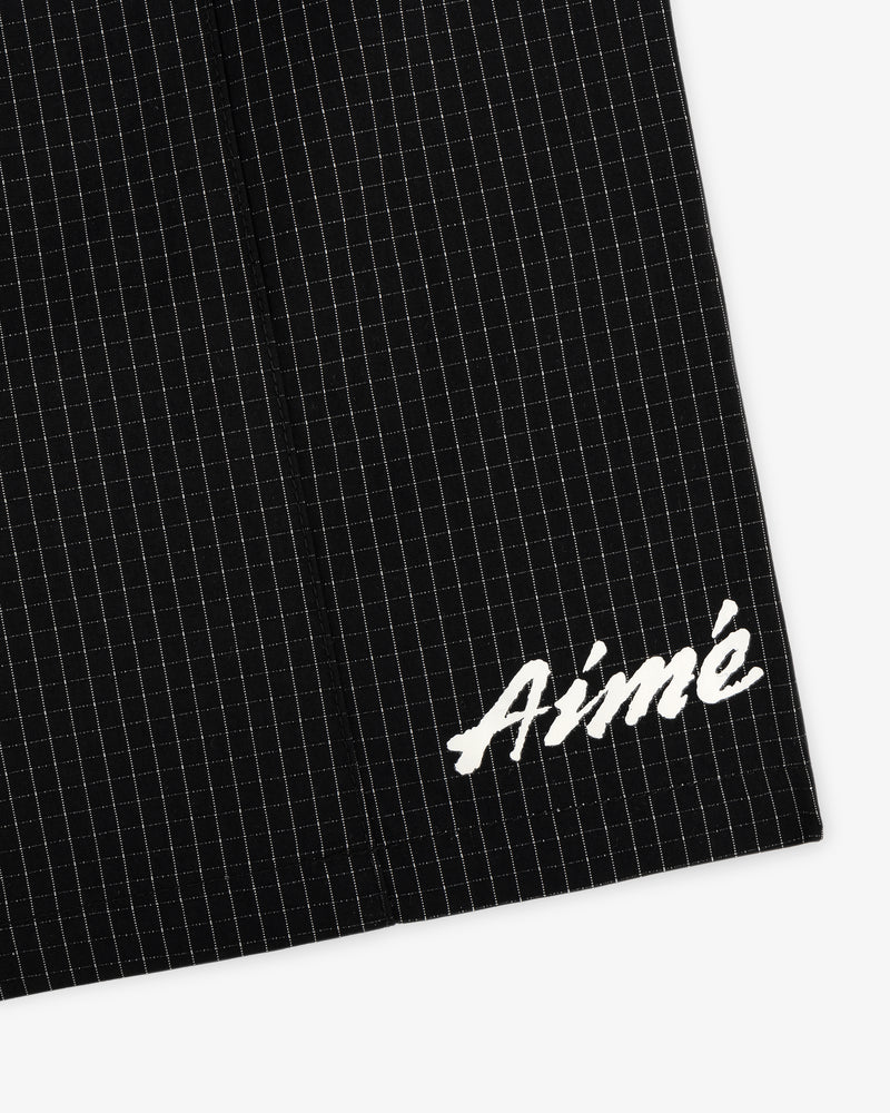 Close-up of Ripstop Nylon Wave Short in black with white grid lines and Aimé embroidered in white script on the lower corner.