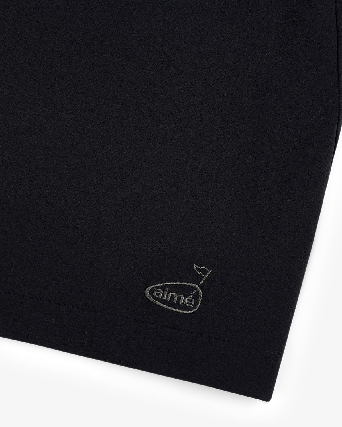 Close-up of ALD Golf Performance Short in black with a small embroidered aimé logo and a wavy line in the corner.