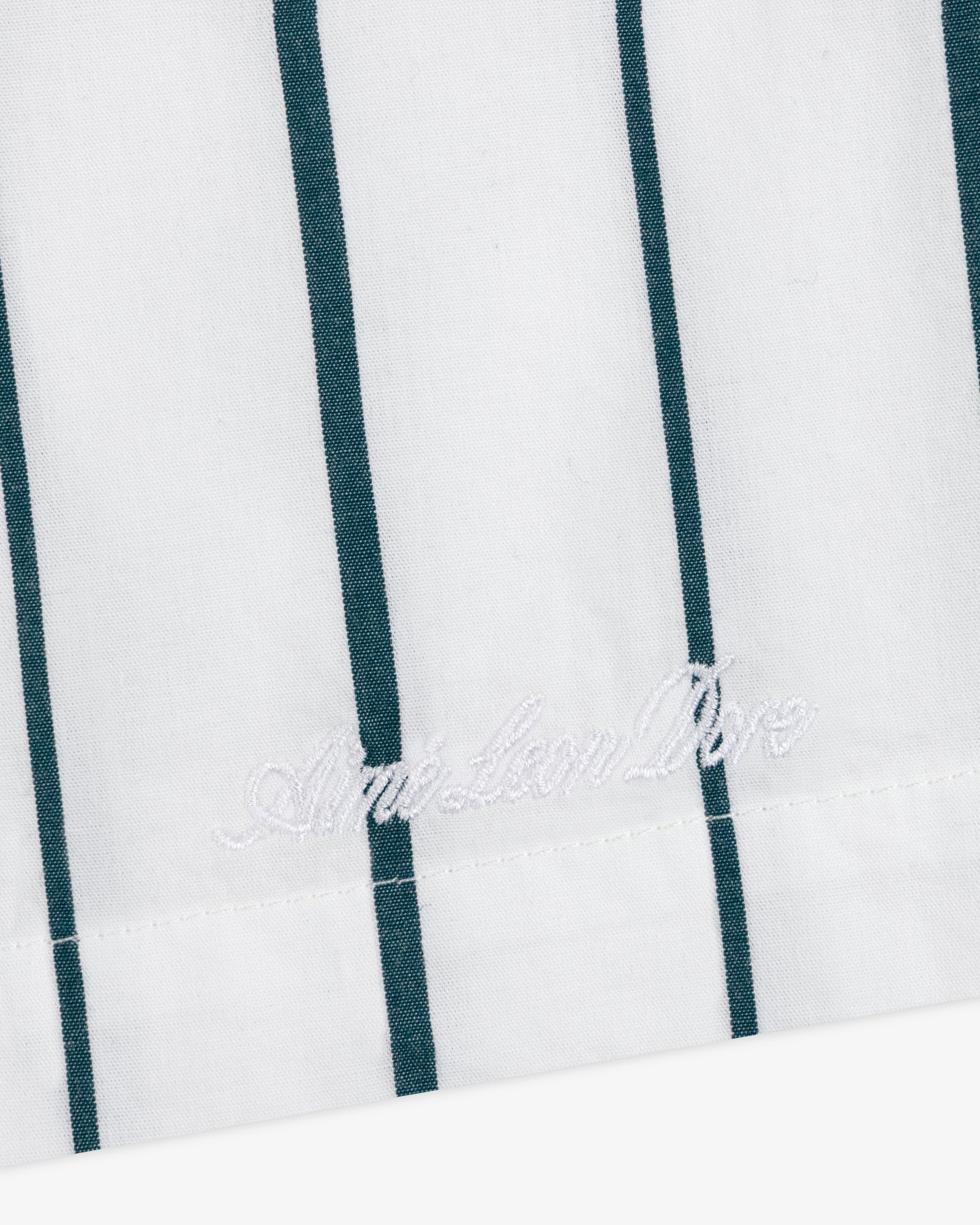 White poplin leisure shorts with vertical green stripes and white "American Dior" embroidery near the edge.