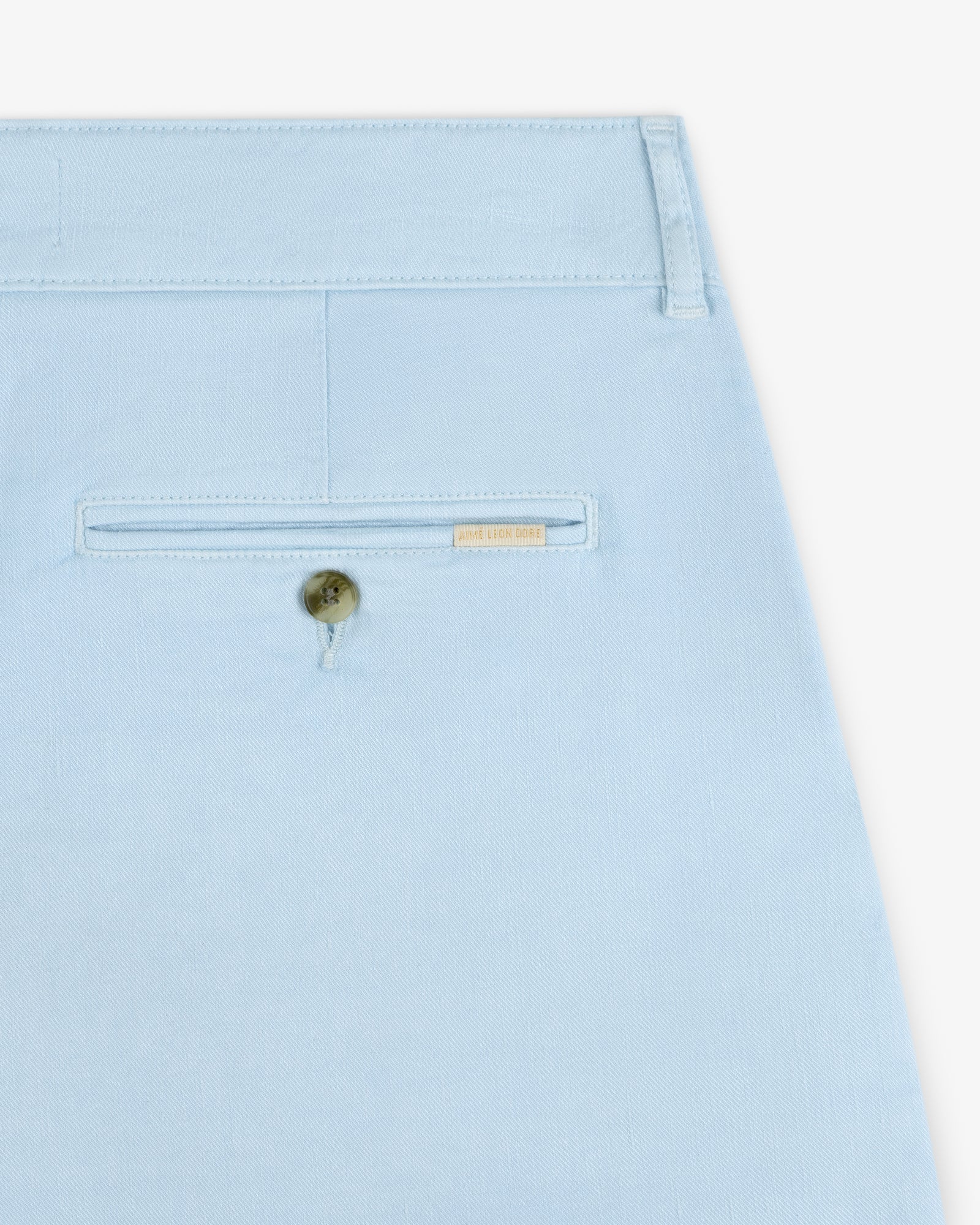 Close-up of the back pocket of Pleated Linen Blend Bermuda Shorts in light blue, with button and beige label above pocket.