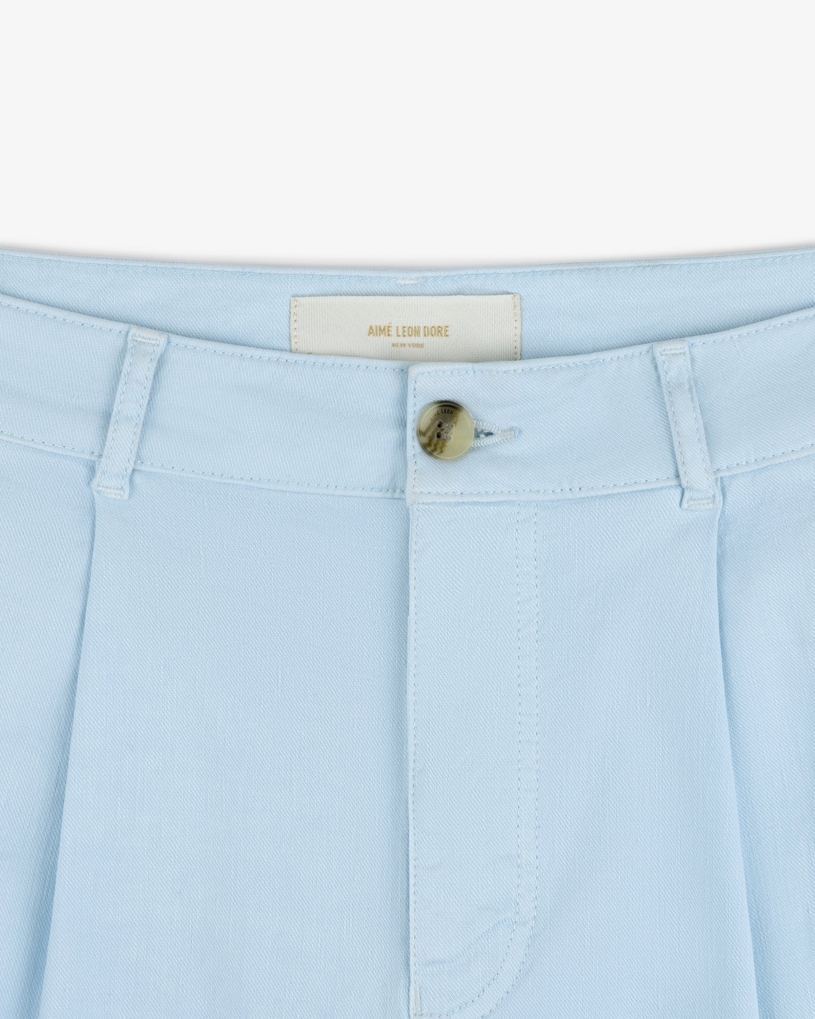 Close-up of Pleated Linen Blend Bermuda Short in light blue with tan button and AIME LEON DORE label inside waistband.