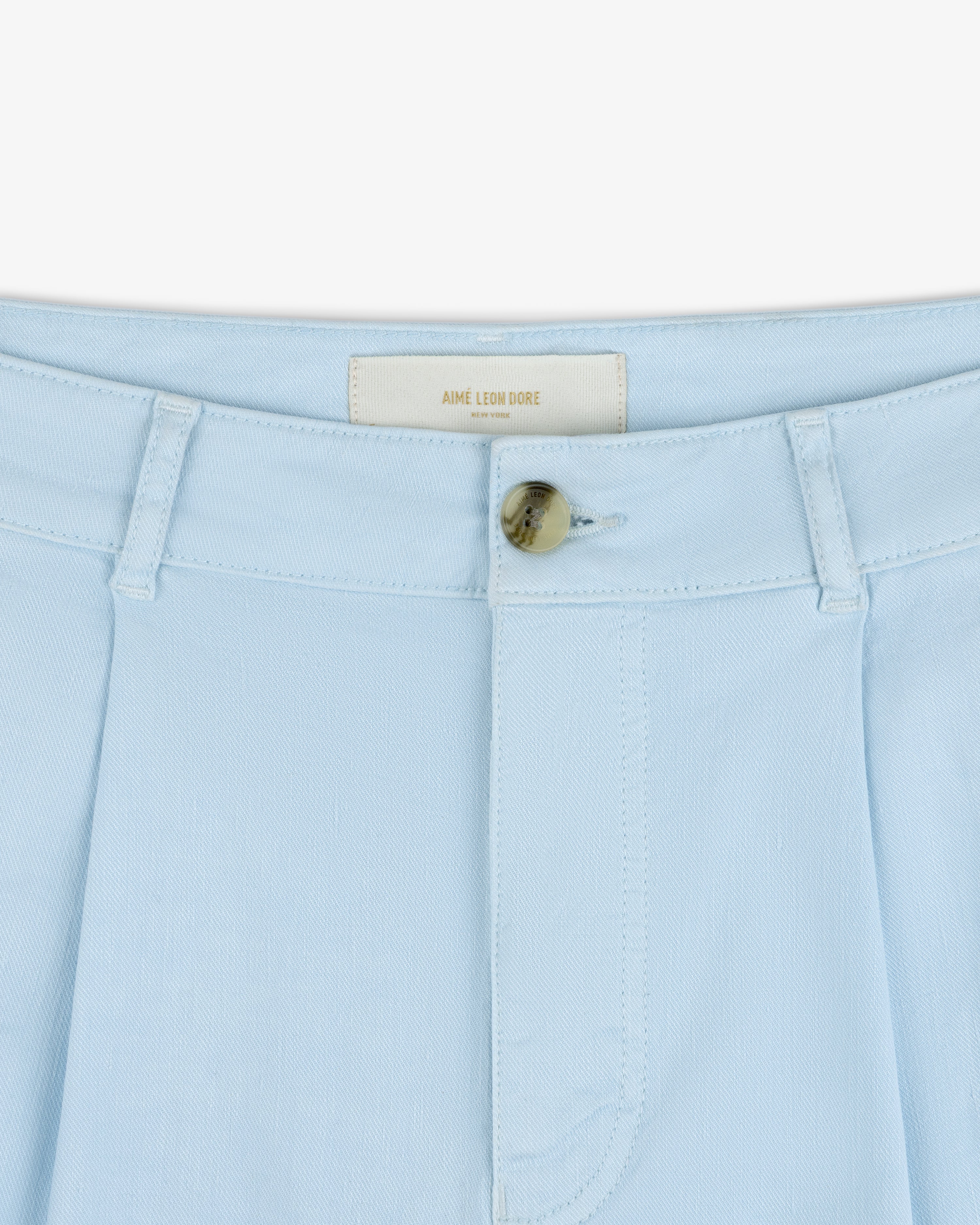 Close-up of Pleated Linen Blend Bermuda Short in light blue with tan button and AIME LEON DORE label inside waistband.