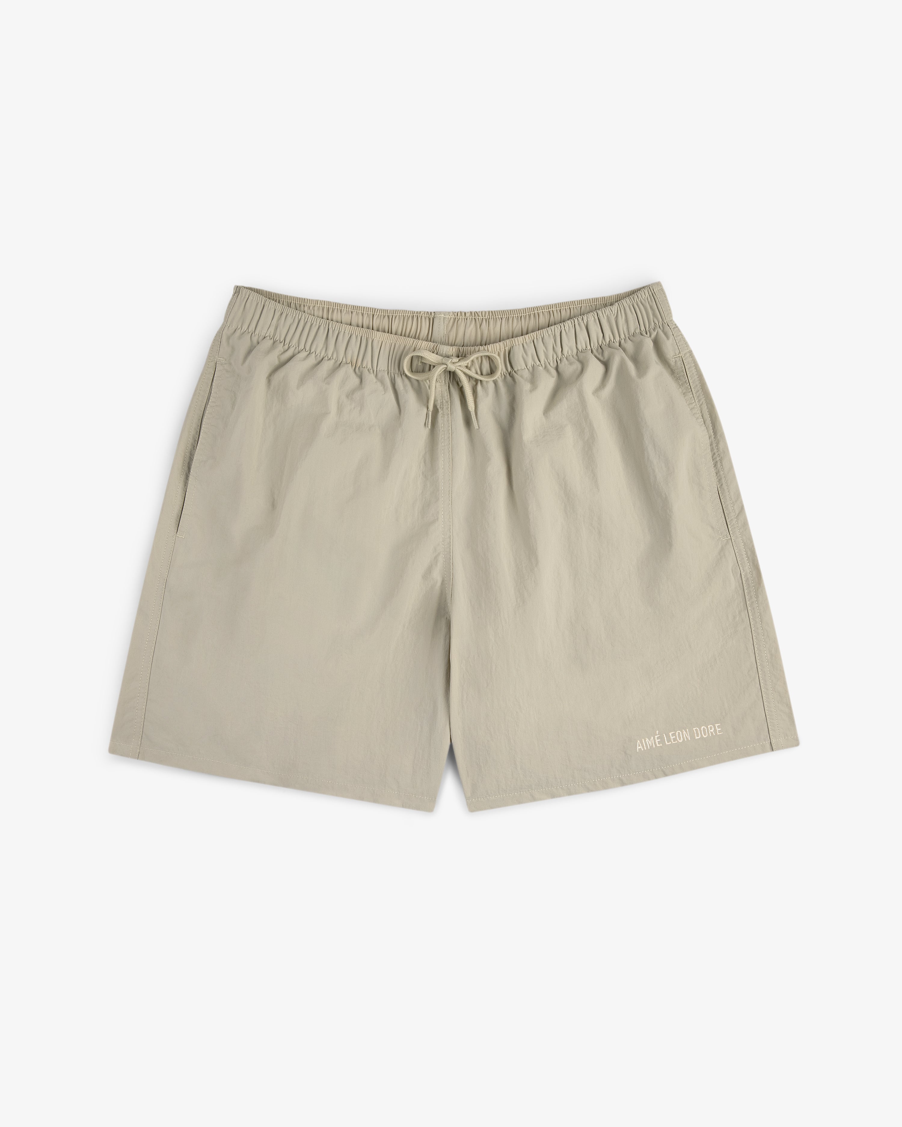 Core Nylon Short in beige with an elastic waistband and AIME LEON DORE text near the left leg hem.