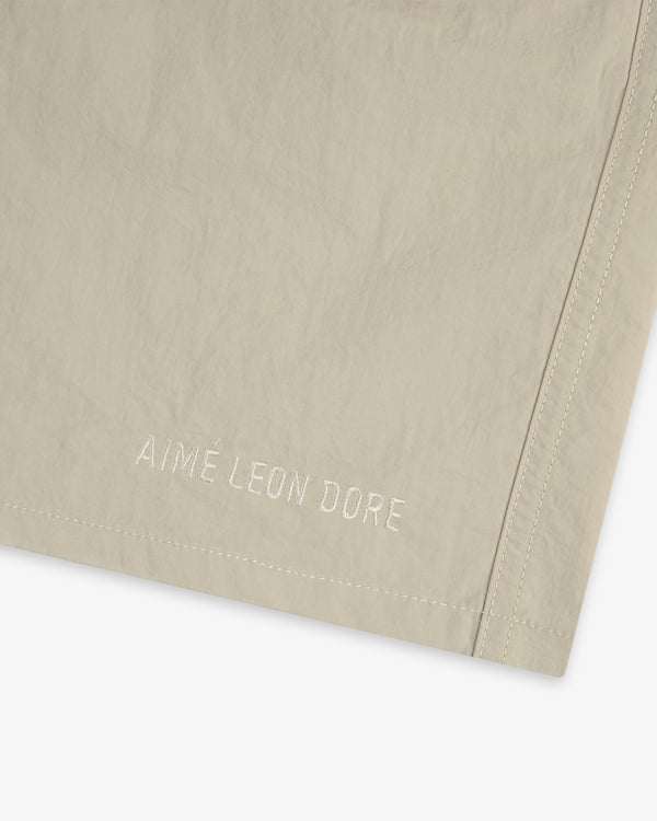 Close-up of beige Core Nylon Short with AIMÉ LEON DORE embroidered in white near the hem.