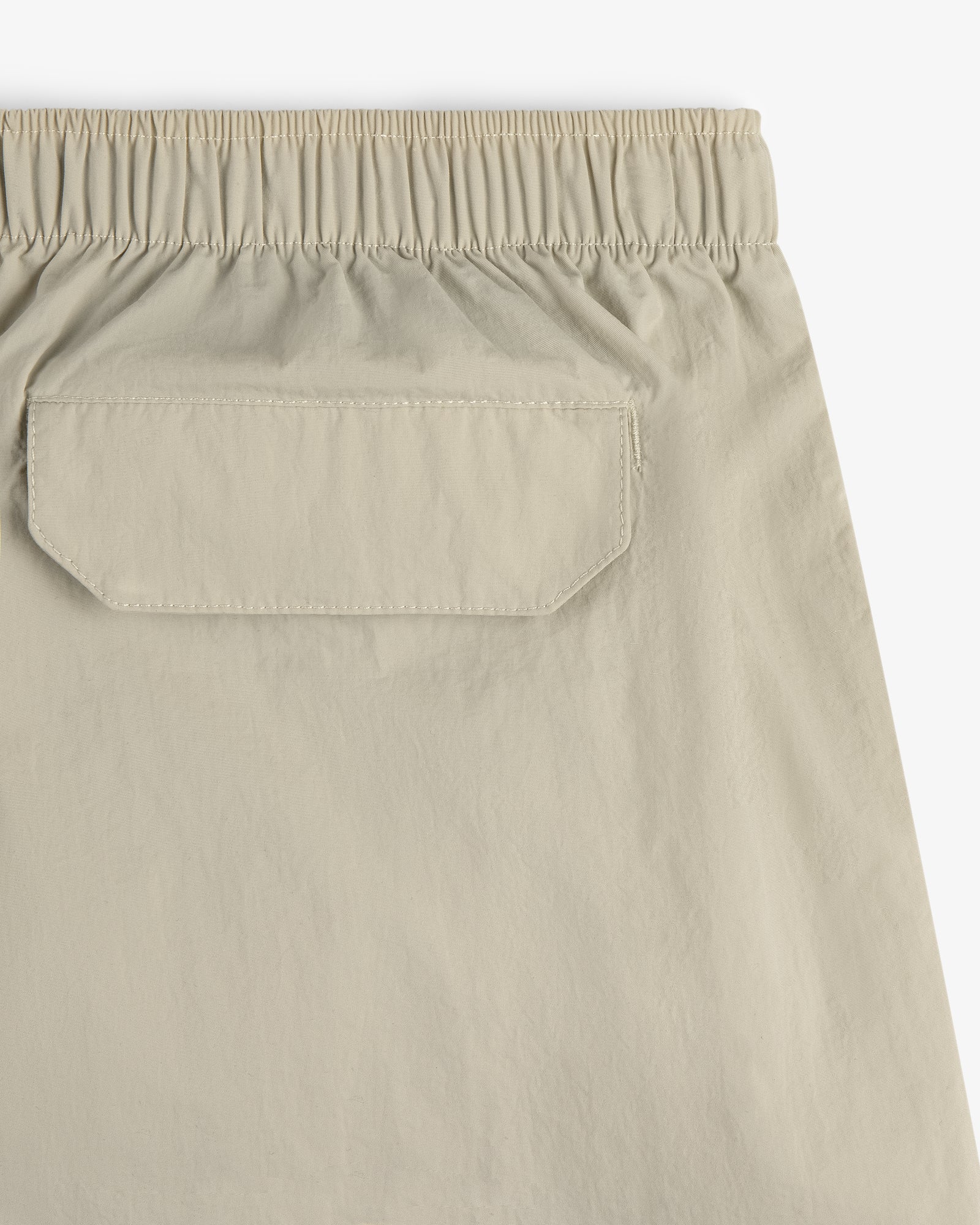 Close-up of Core Nylon Short in beige, featuring an elastic waistband and a back flap pocket.