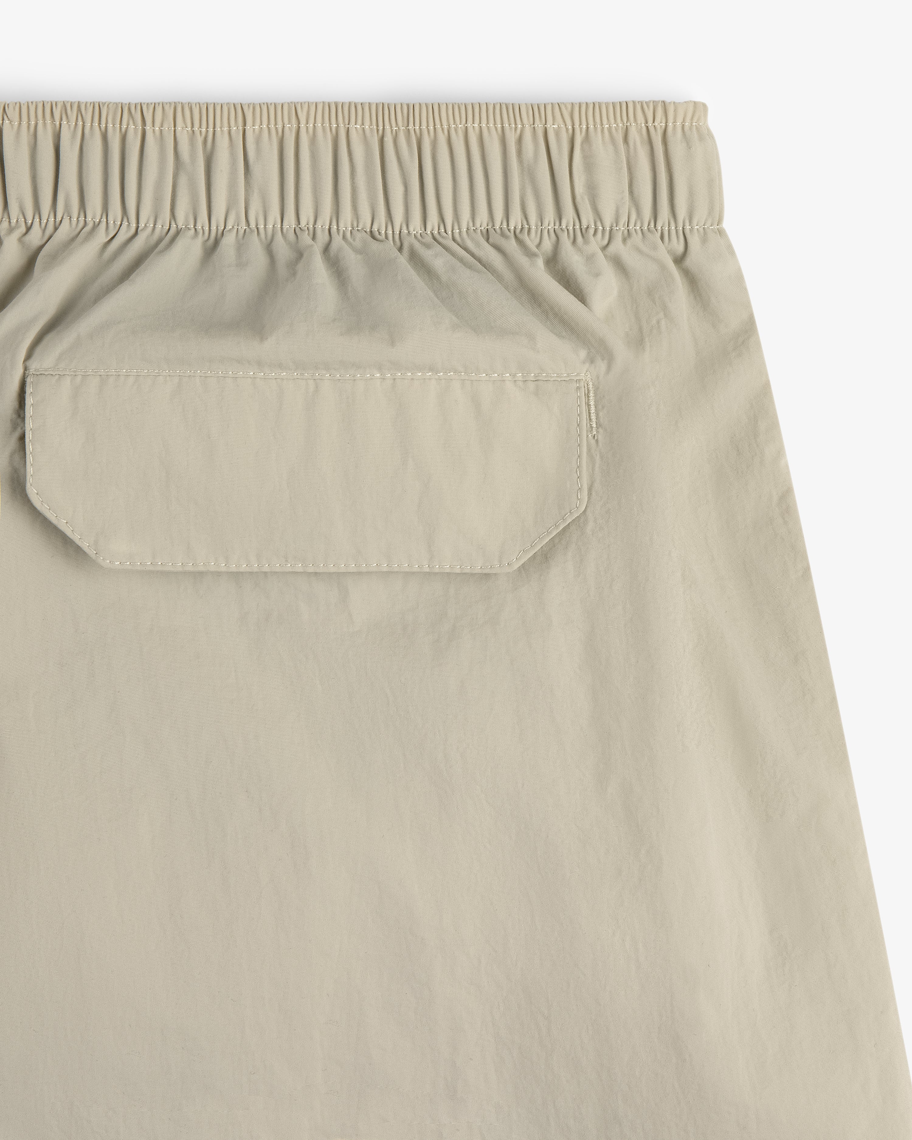 Close-up of Core Nylon Short in beige, featuring an elastic waistband and a back flap pocket.