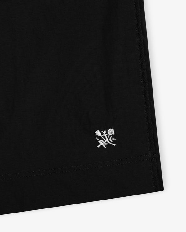 Close-up of the Long Nylon Track Short in black, showing a small white flower and leaf embroidered near the hem.