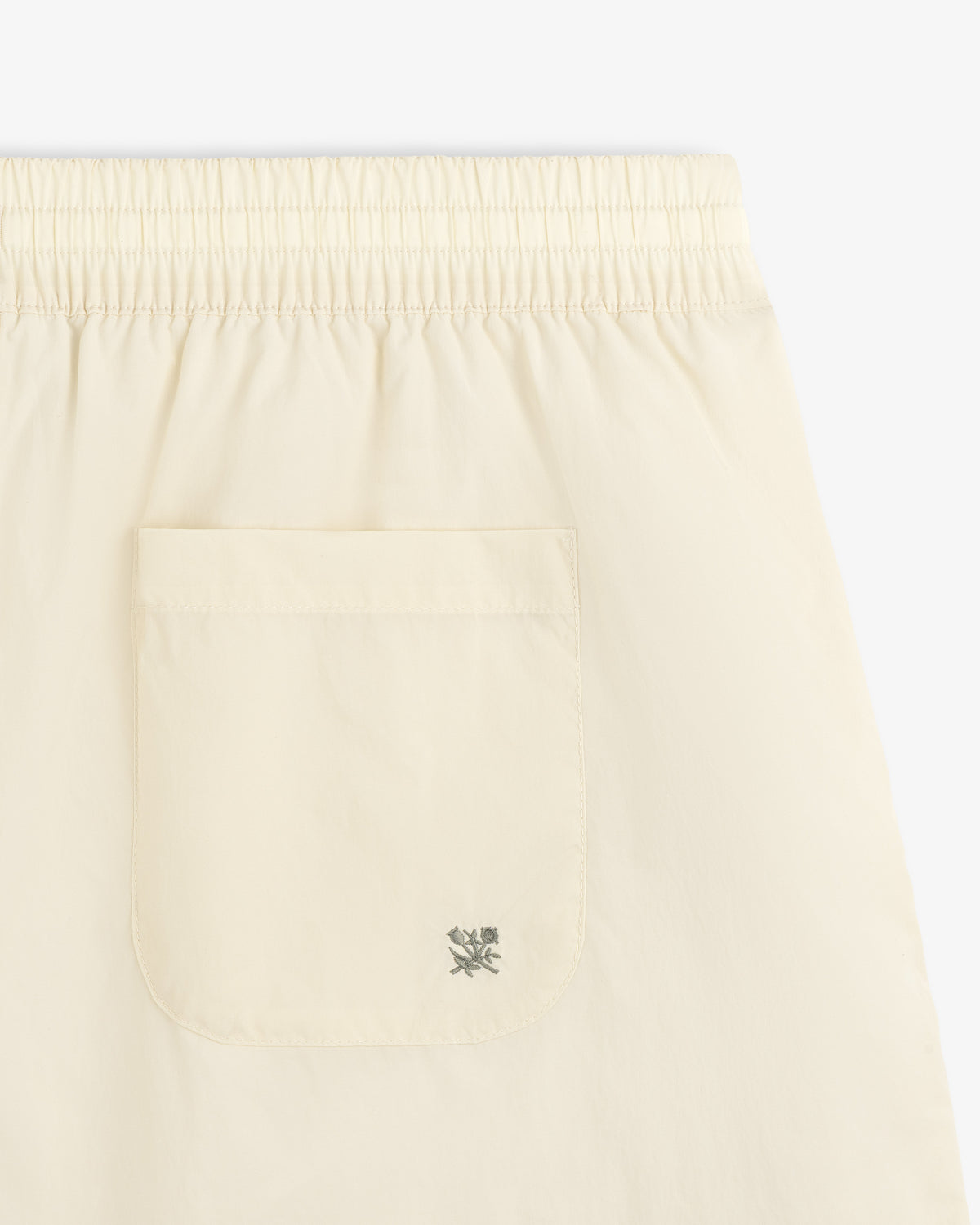 Close-up of Long Nylon Track Short in light yellow with elastic waistband and back pocket featuring a small logo.