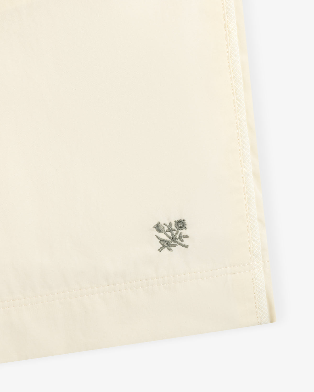 Close-up of Long Nylon Track Short in cream with a small embroidered bird and flower near the hem.