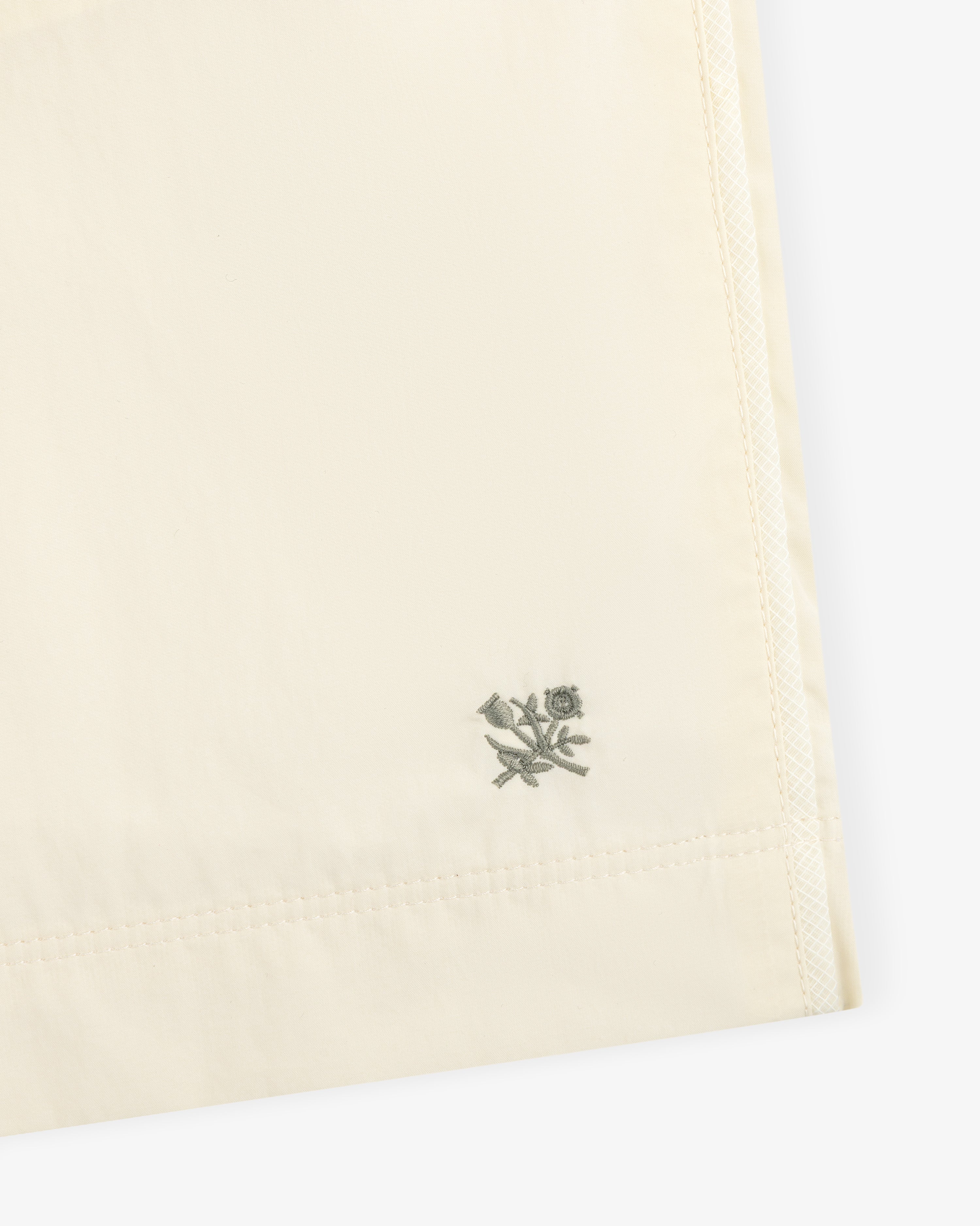 Close-up of Long Nylon Track Short in cream with a small embroidered bird and flower near the hem.