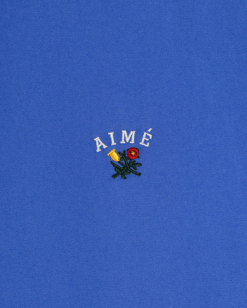 Blue Leon Overshirt with AIMÉ embroidered above a yellow and red flower with green leaves.