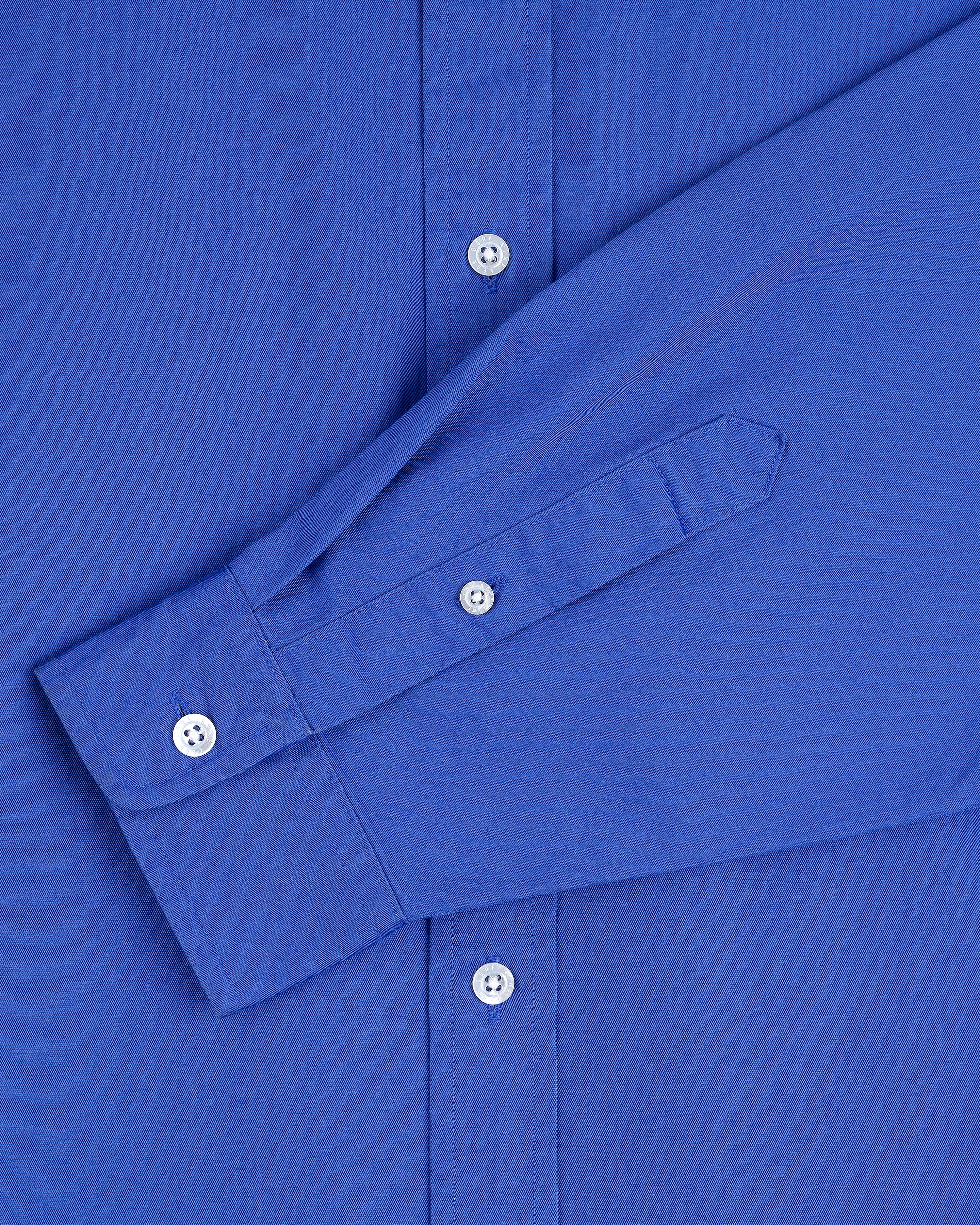 Close-up of the Leon Overshirt, a long-sleeve blue button-up with white buttons, showing the front and sleeve.
