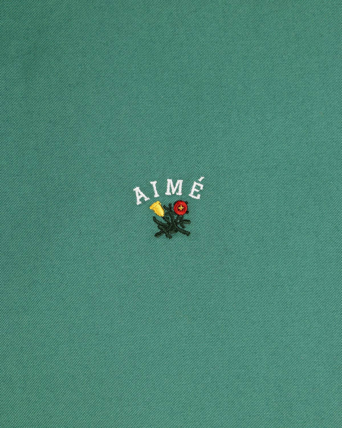 Green Leon Overshirt with AIMÉ text above embroidered yellow and red flowers with green leaves.