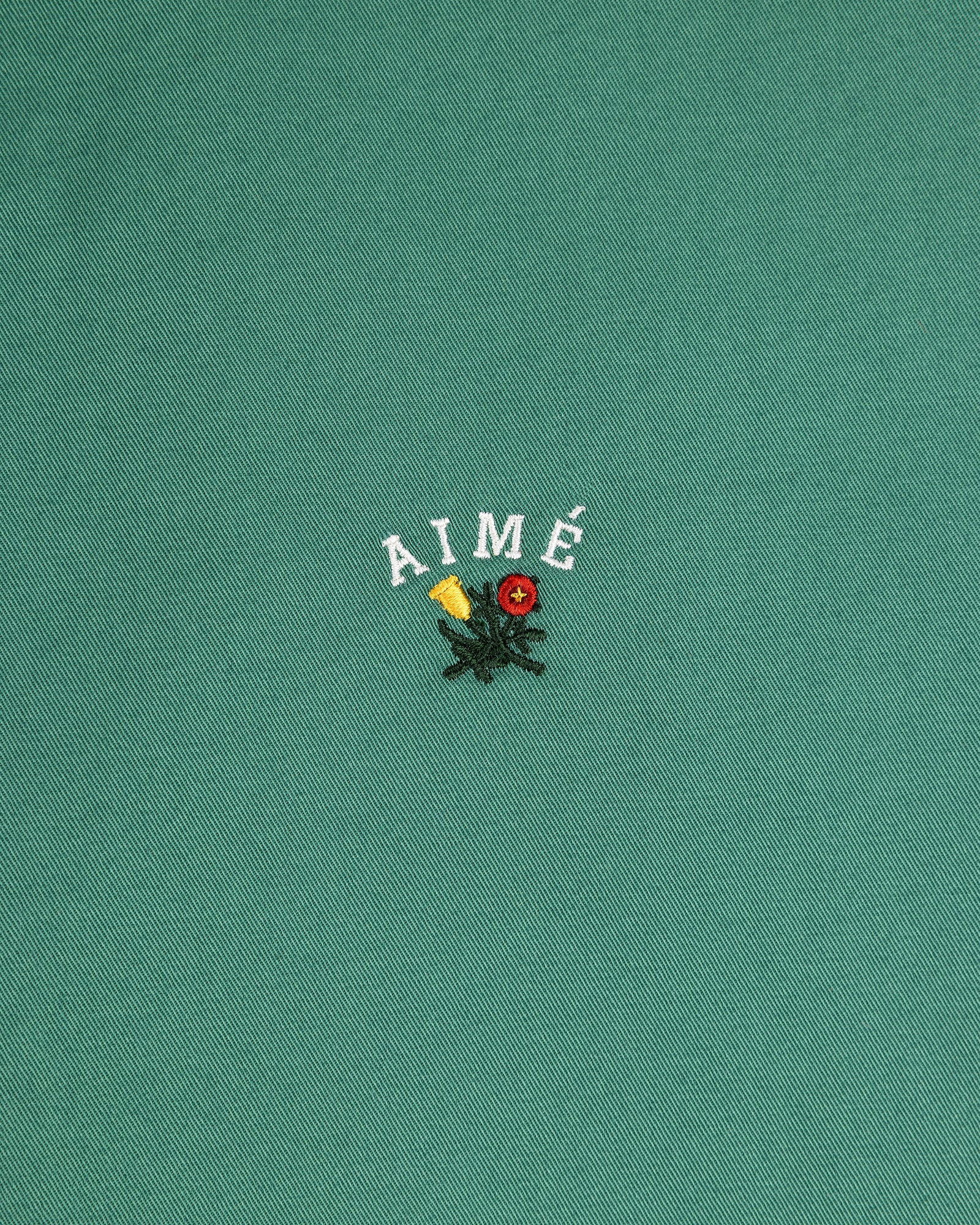 Green Leon Overshirt with AIMÉ text above embroidered yellow and red flowers with green leaves.