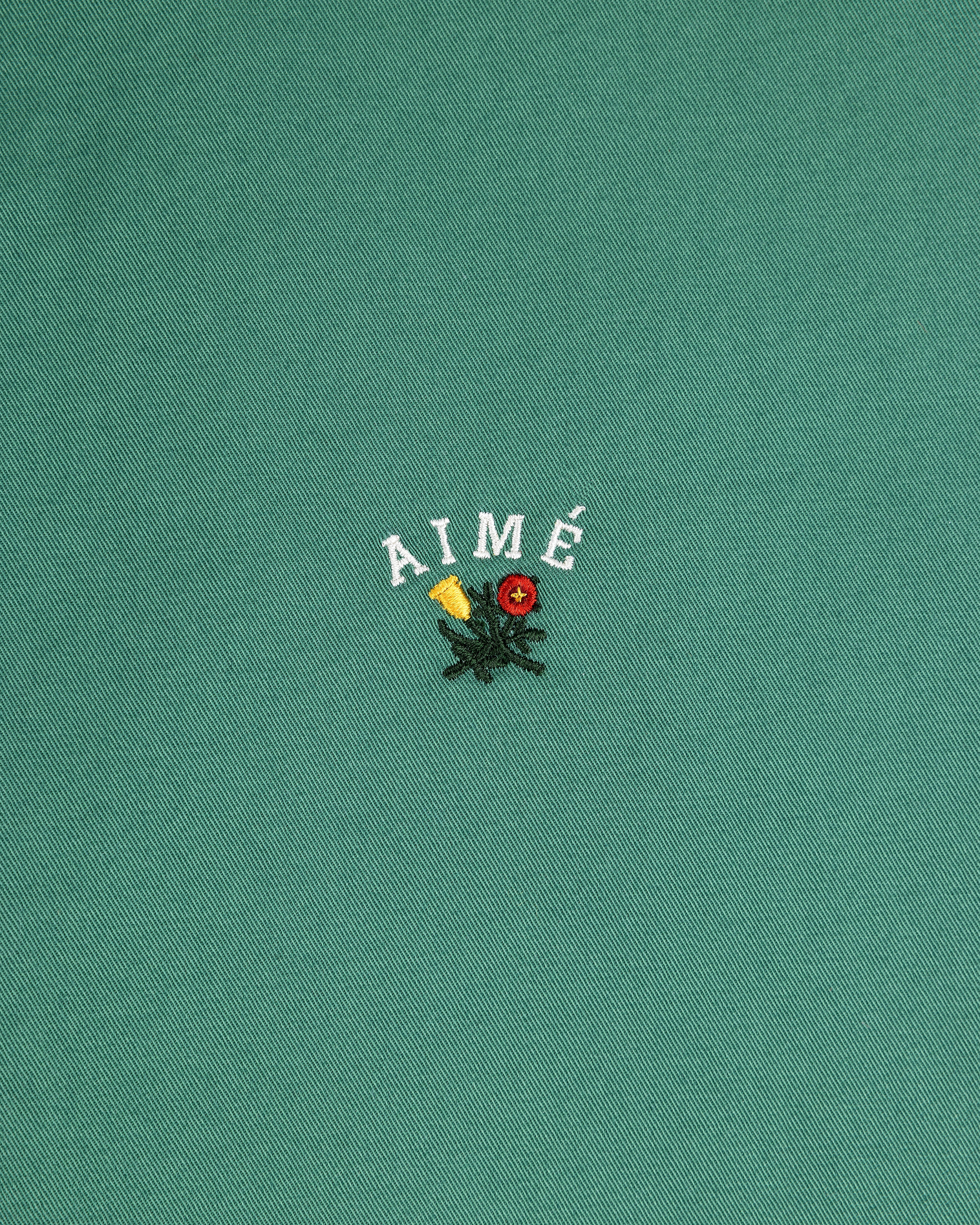 Green Leon Overshirt with AIMÉ text above embroidered yellow and red flowers with green leaves.