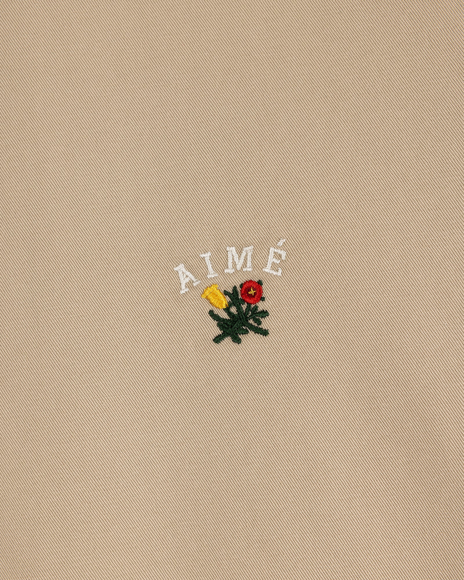 Beige Leon Overshirt with "AIMÉ" text and embroidered yellow, red flowers with green leaves below the lettering.