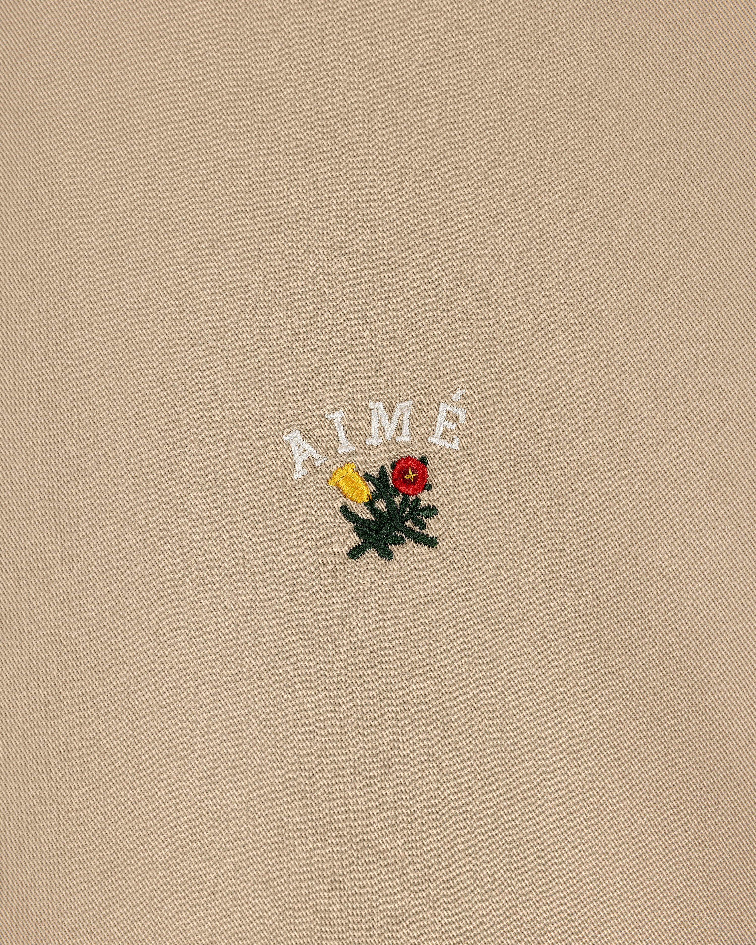 Beige Leon Overshirt with "AIMÉ" text and embroidered yellow, red flowers with green leaves below the lettering.