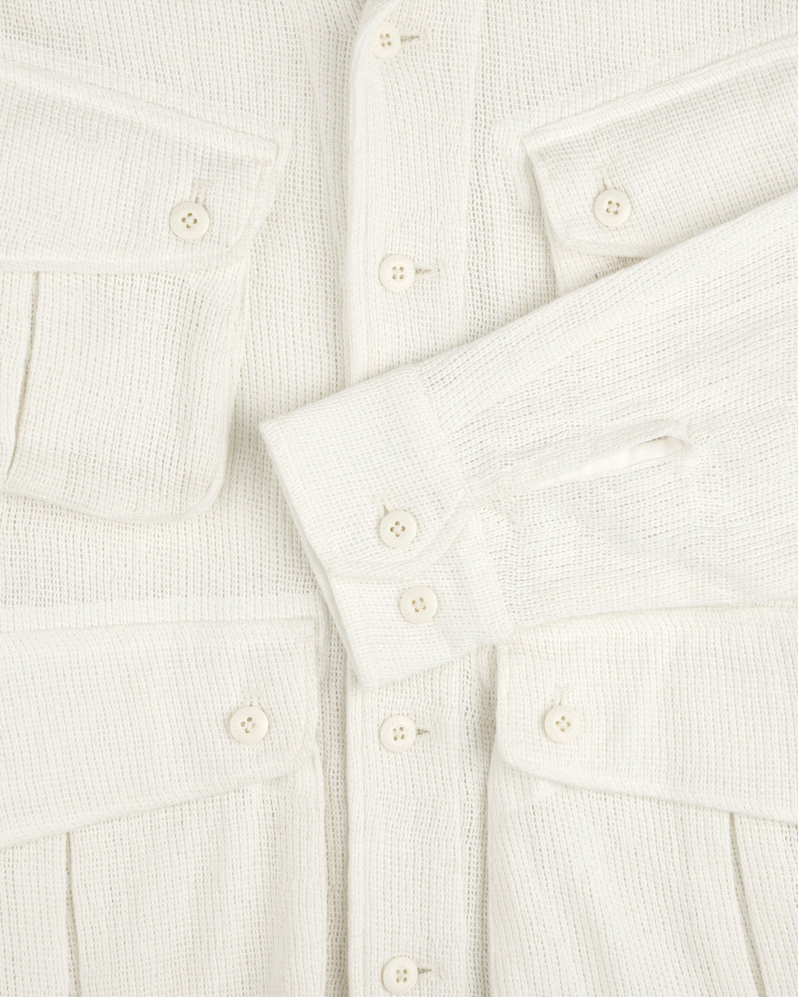 Close-up of the Mesh Jungle Shirt: textured cream fabric, white buttons, two chest pockets, one sleeve across the front.