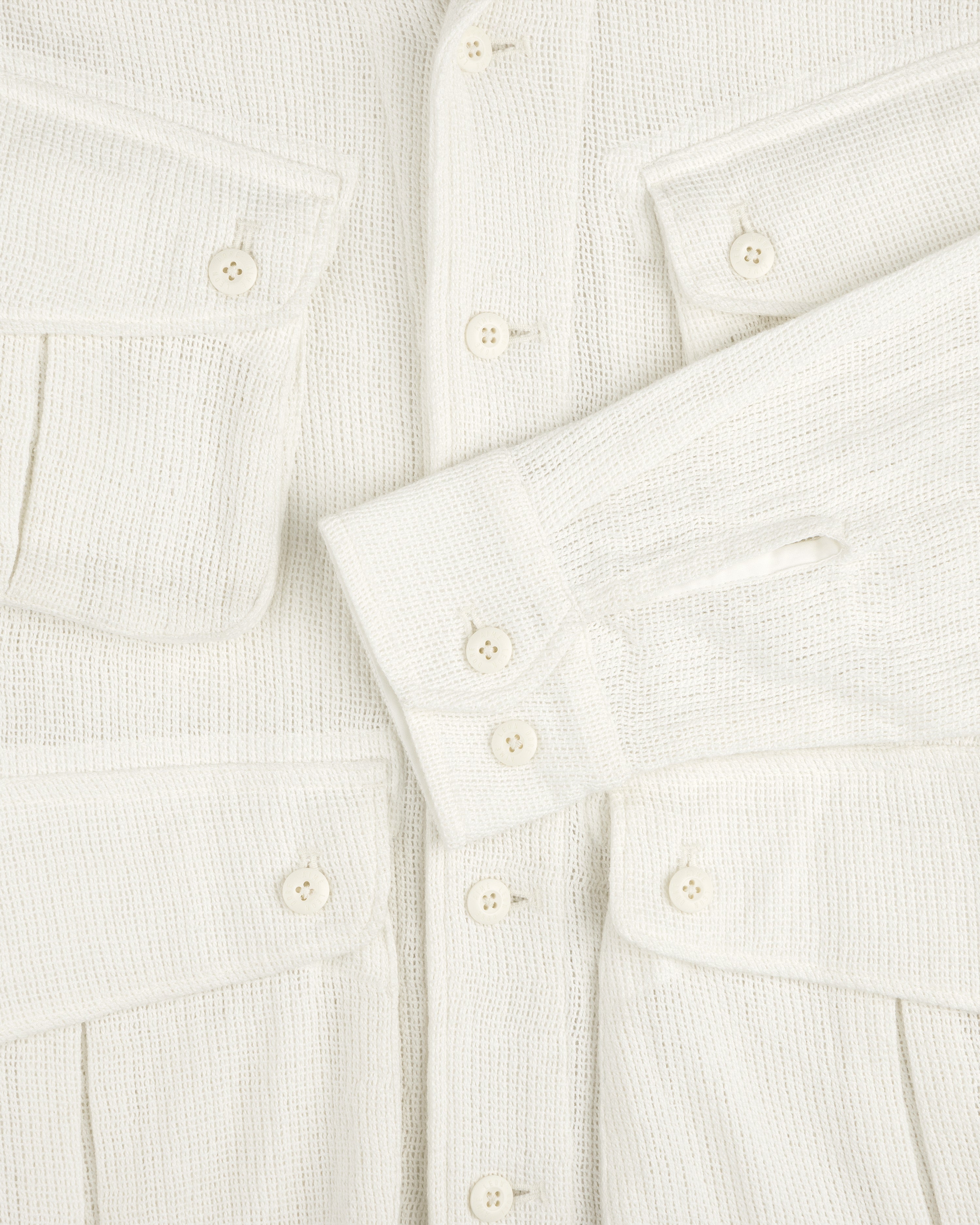 Close-up of the Mesh Jungle Shirt: textured cream fabric, white buttons, two chest pockets, one sleeve across the front.
