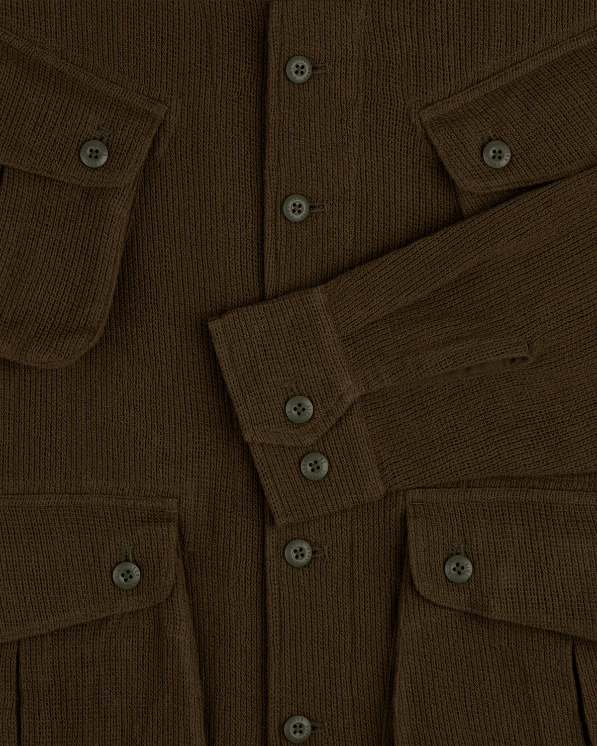 Close-up of the Mesh Jungle Shirt, a brown ribbed knit with buttons, flap pockets, and one sleeve folded across the front.