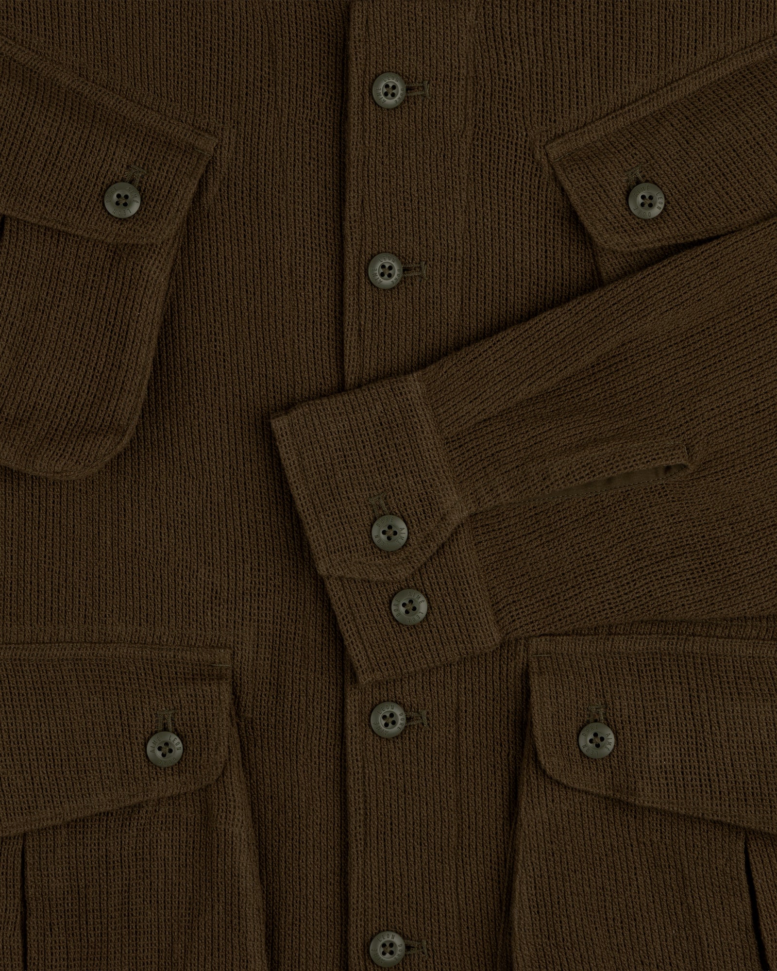 Close-up of the Mesh Jungle Shirt, a brown ribbed knit with buttons, flap pockets, and one sleeve folded across the front.