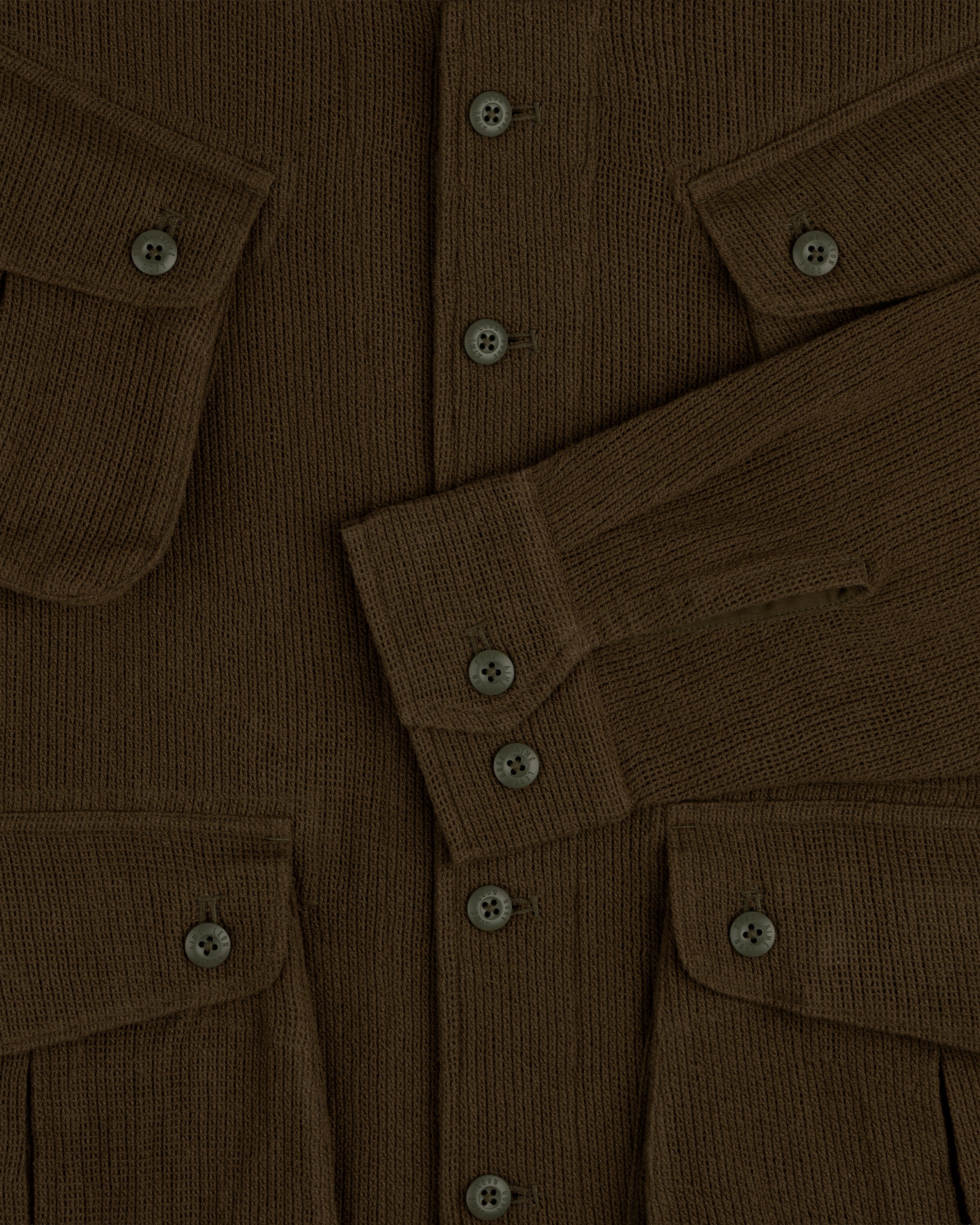 Close-up of the Mesh Jungle Shirt, a brown ribbed knit with buttons, flap pockets, and one sleeve folded across the front.