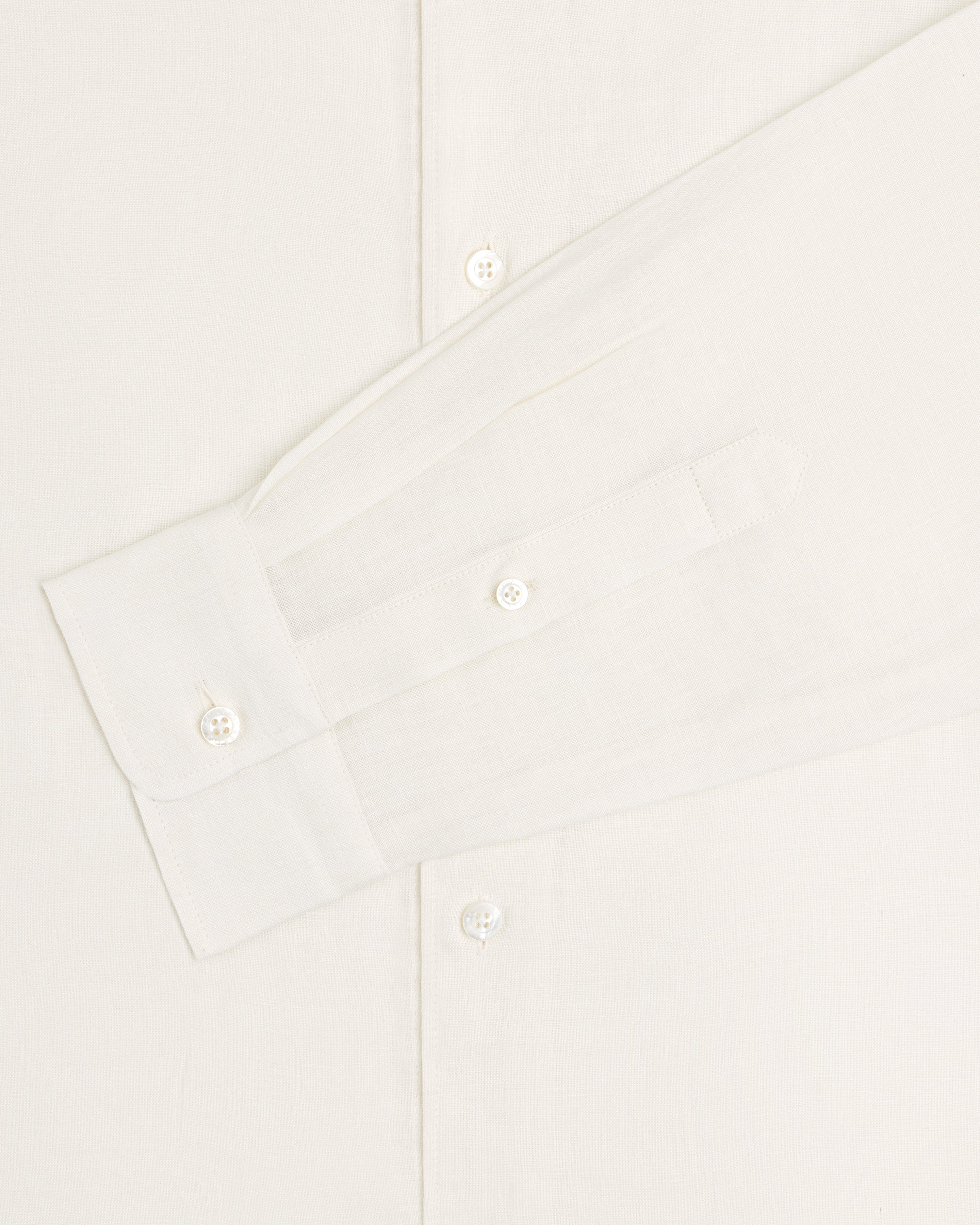 A close-up of the Long-Sleeve Linen Shirt in white, showing its buttons and cuff against a plain background.