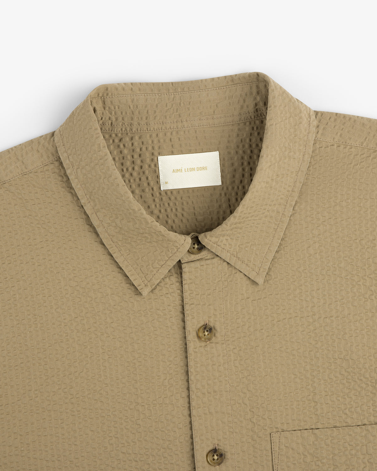 Close-up of a beige Short-Sleeve Seersucker Shirt with a pointed collar, textured fabric, and chest pocket.