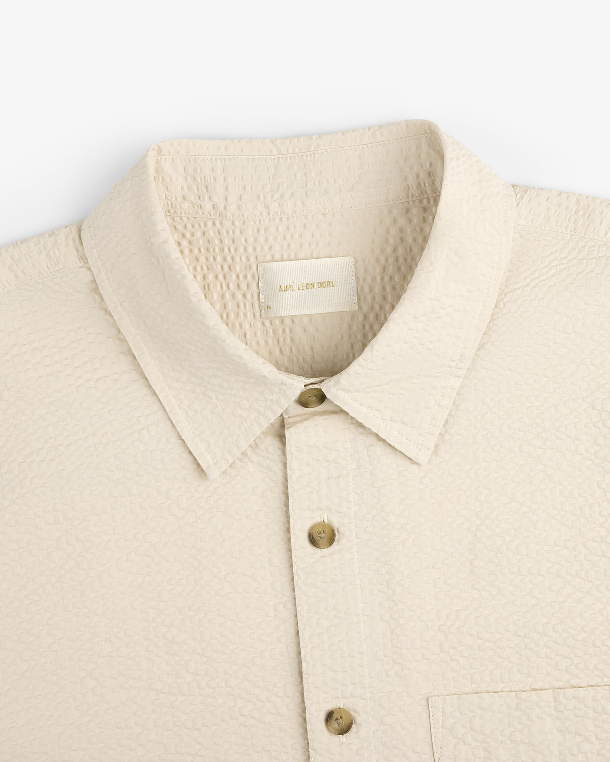 Close-up of a cream-colored Short-Sleeve Seersucker Shirt with textured fabric, collar, and chest pocket.