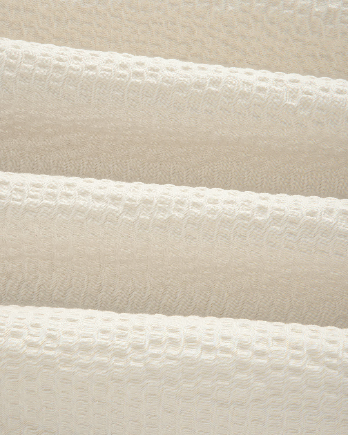 Close-up of cream-colored, textured seersucker fabric with a subtle grid pattern from our Short-Sleeve Seersucker Shirt.