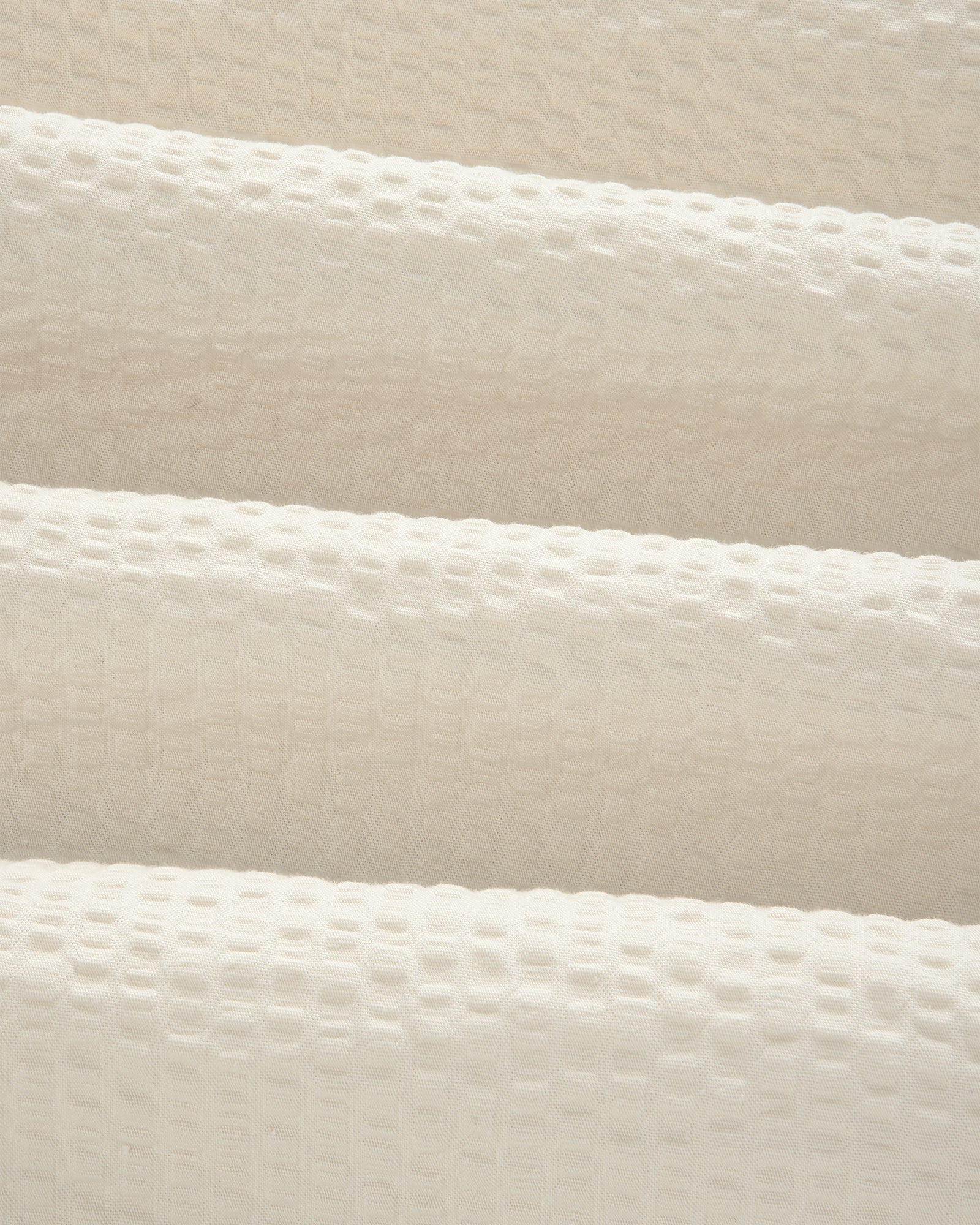 Close-up of cream-colored, textured seersucker fabric with a subtle grid pattern from our Short-Sleeve Seersucker Shirt.
