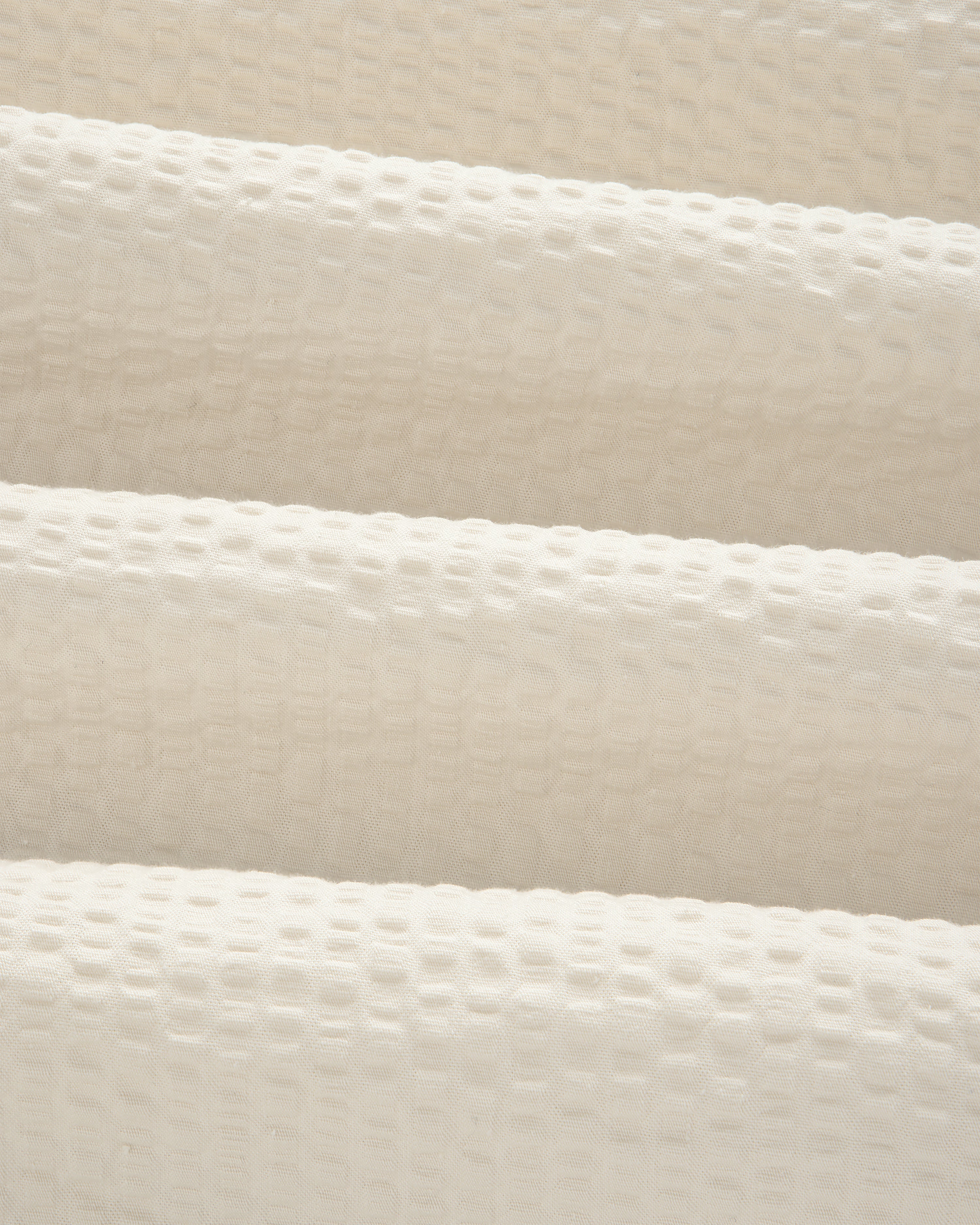 Close-up of cream-colored, textured seersucker fabric with a subtle grid pattern from our Short-Sleeve Seersucker Shirt.