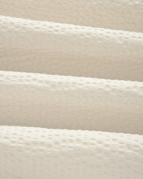 Close-up of cream-colored, textured seersucker fabric with a subtle grid pattern from our Short-Sleeve Seersucker Shirt.