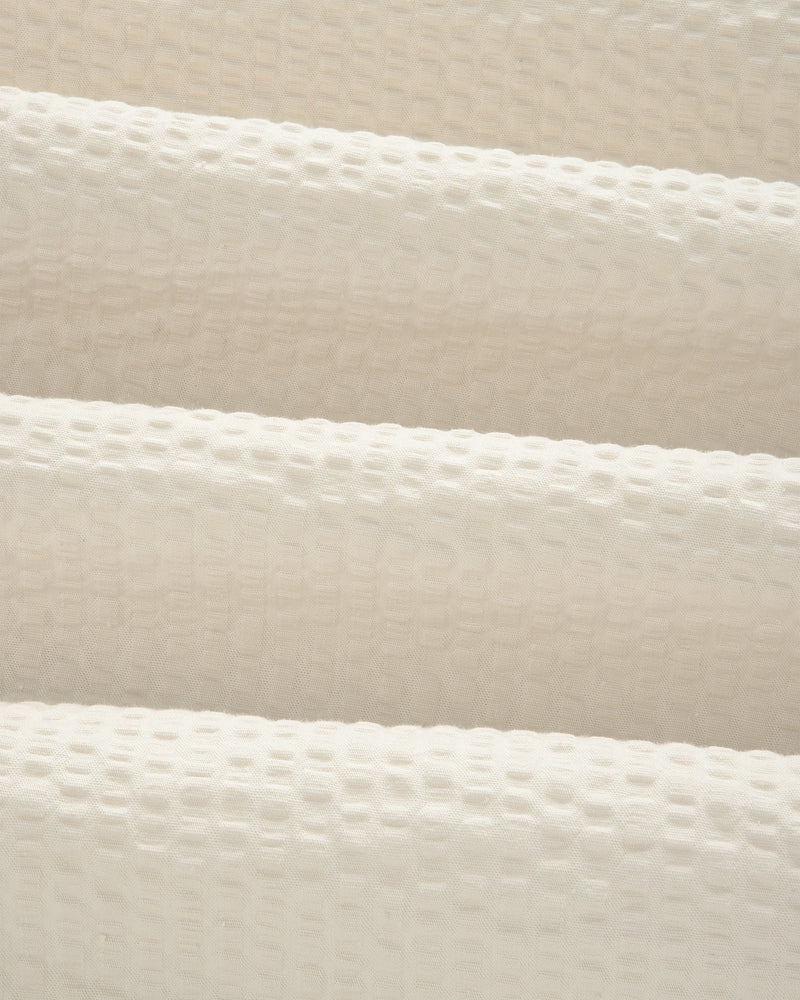 Close-up of cream-colored, textured seersucker fabric with a subtle grid pattern from our Short-Sleeve Seersucker Shirt.
